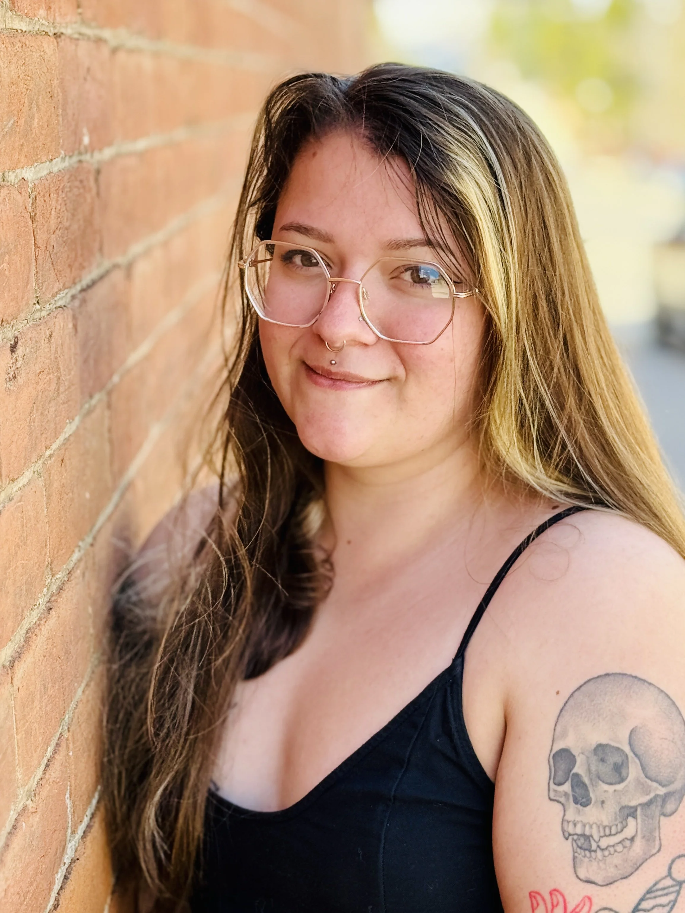 A portrait-style photograph shows Sydni from the chest up, leaning her back against a textured, light reddish-brown brick wall on the left side of the frame.