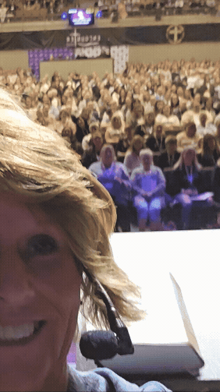 Alora Hosfield speaking at a conference with a large audience seated in front of her.