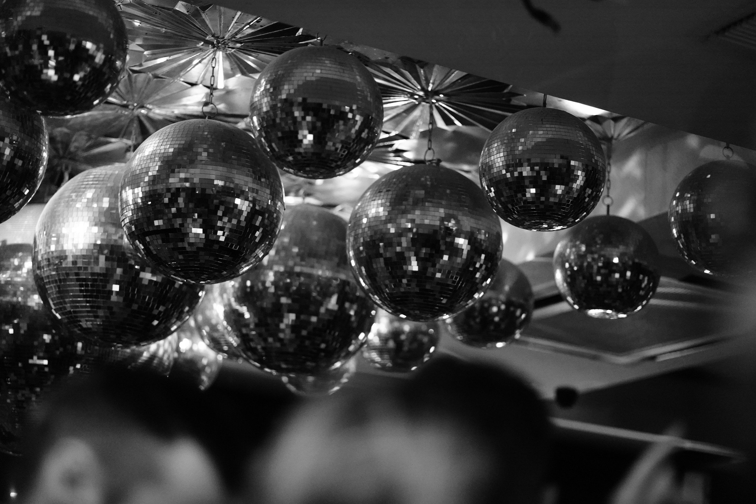 Black and white photo of multiple disco balls hanging from the ceiling, reflecting light and creating a glittering effect.