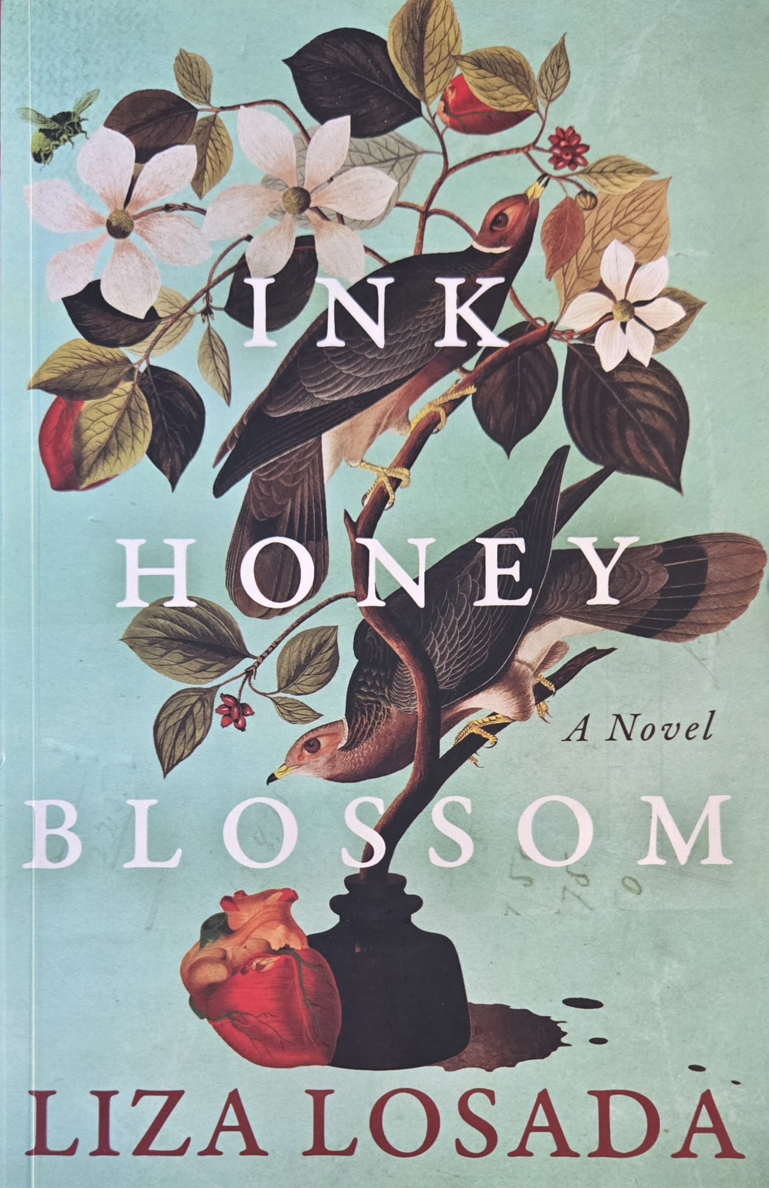 The book cover features an illustration of a branch with white flowers, leaves, and berries. Two birds, one with a reddish head and the other mostly black, are perched on the branch. There is a black vase at the bottom, with a red heart-shaped object and black ink splatters. The title reads "INK HONEY BLOSSOM" and the author's name is Lizá Losadá.