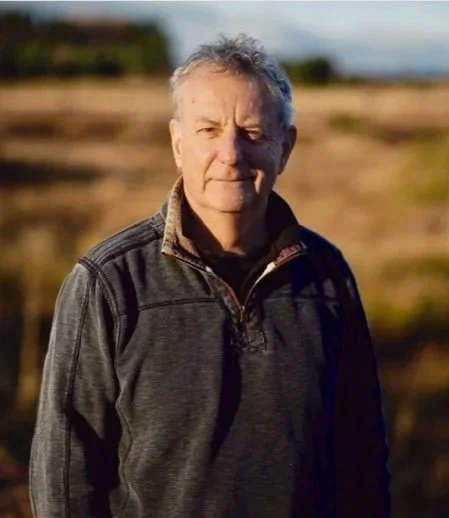 Jeremy Leggett, Founder and CEO of NatureProsperity, solar pioneer and social entrepreneur. Standing outdoors in a field during sunset, wearing a dark gray jacket.