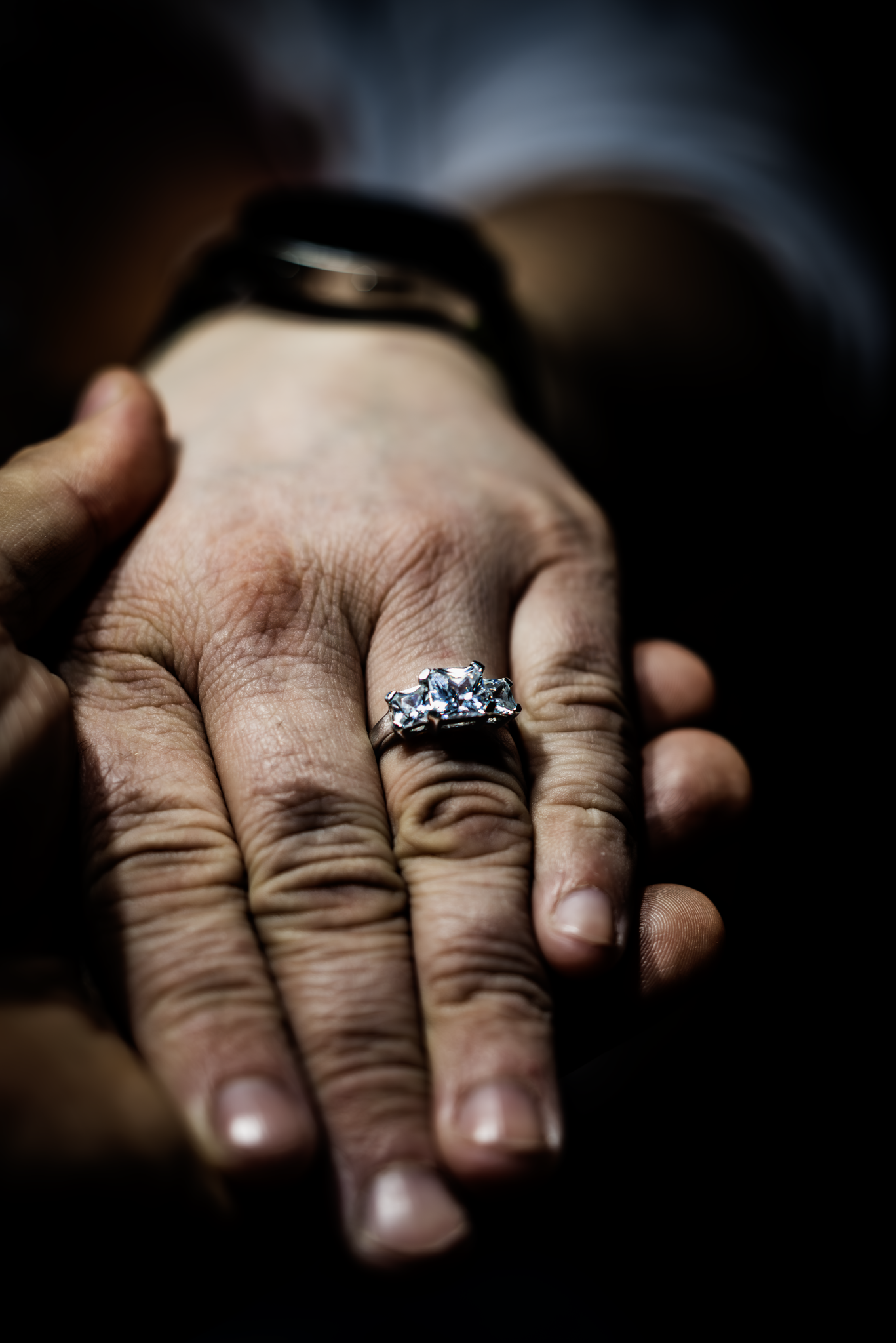 A close-up of a hand wearing a wedding ring with a large central gemstone, pointing to a finger.