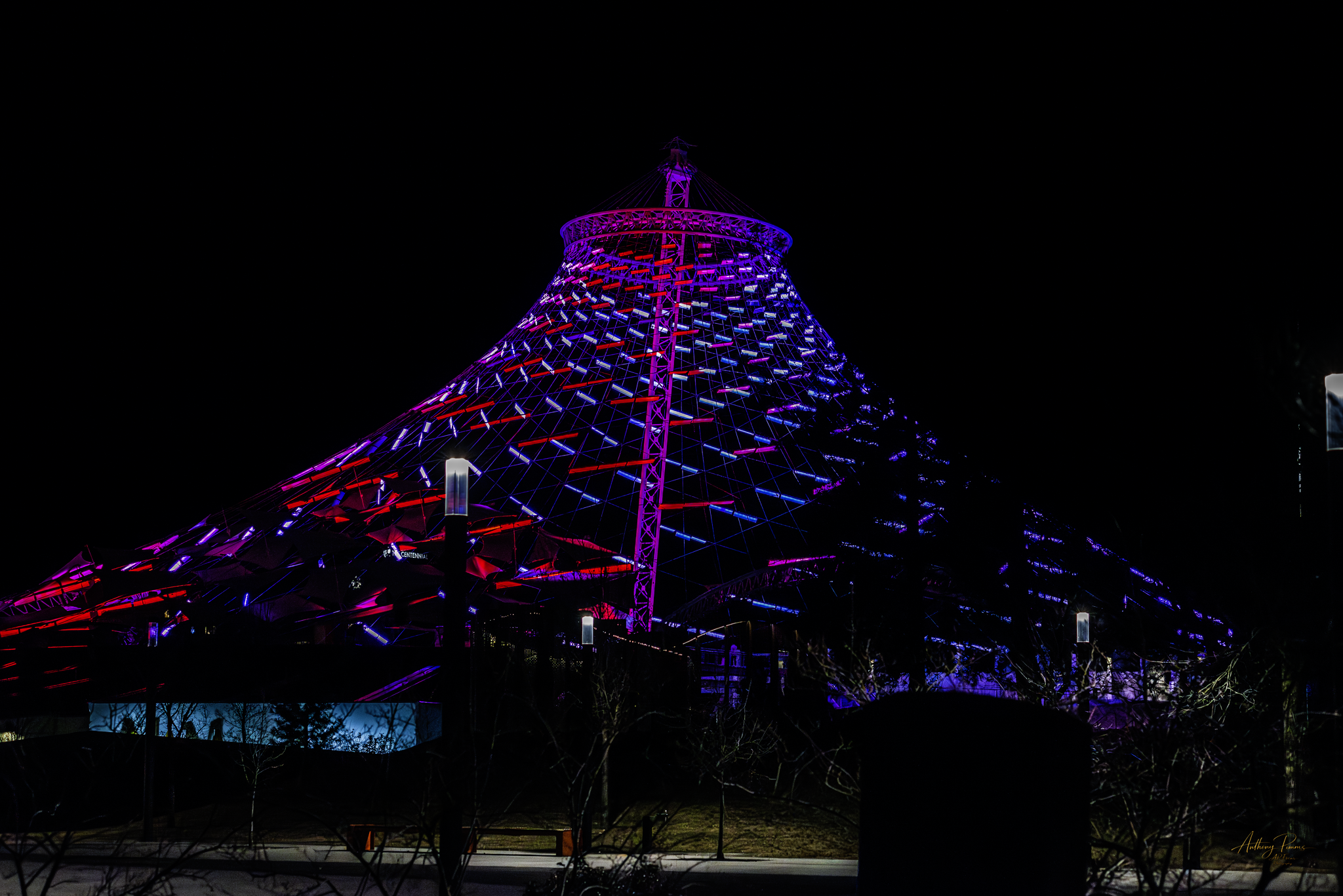 Night view of a modern, illuminated tower with purple and red lights against a dark sky.