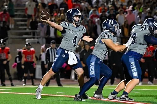 American football quarterback preparing to throw the ball, with teammates in formation on the field.