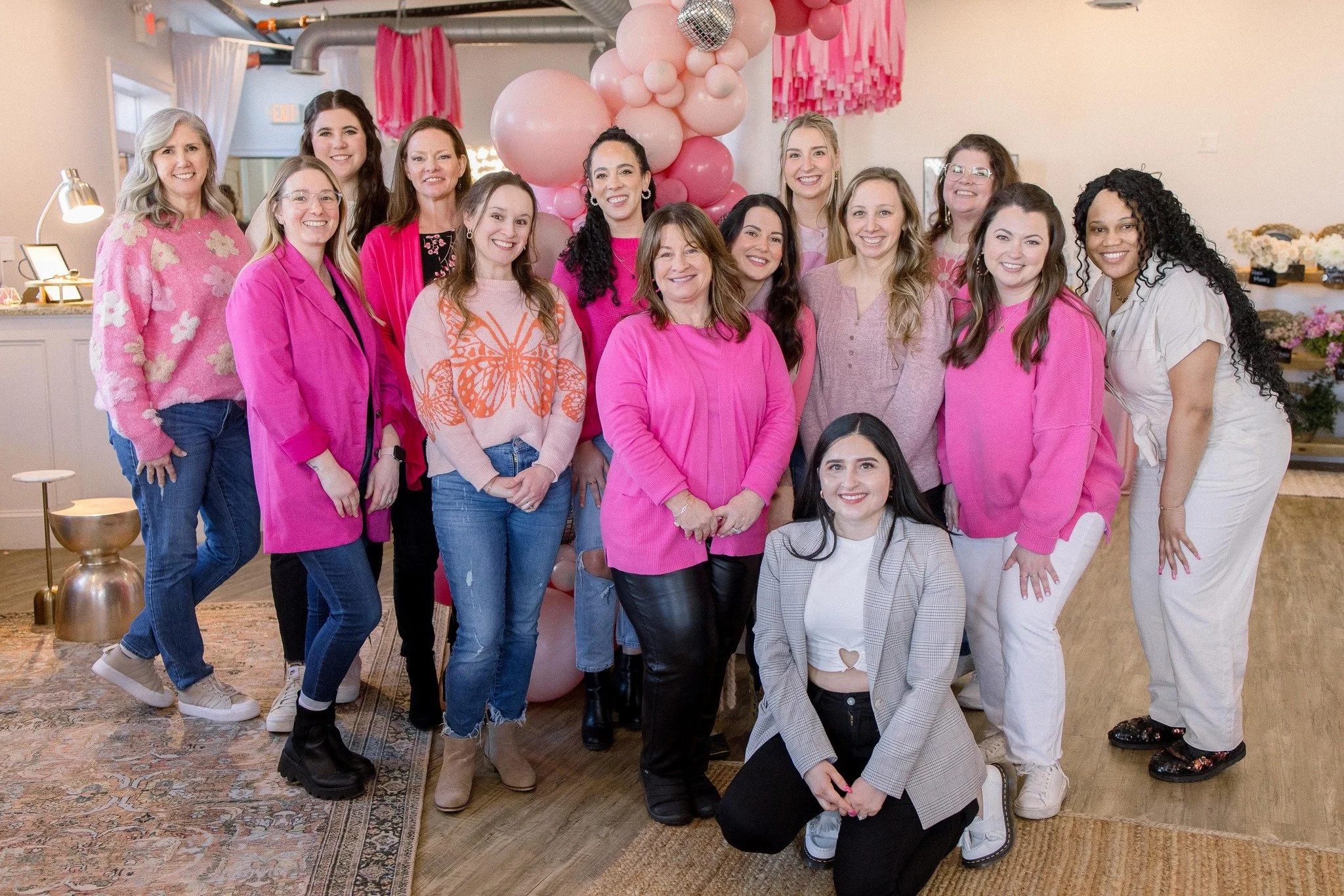 Group of women smiling at a celebration with pink balloons in the background.