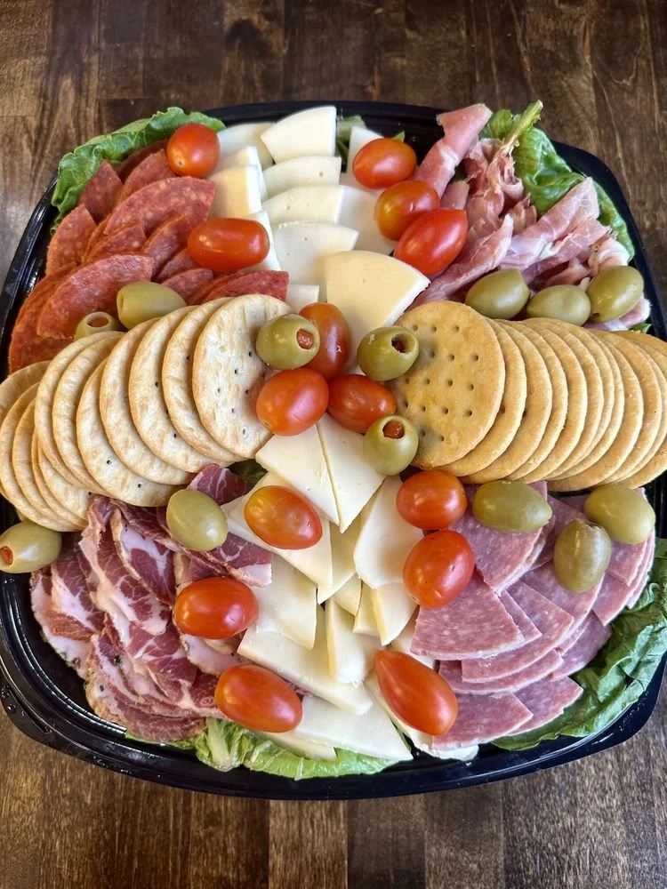 A platter of assorted meats, cheeses, cherry tomatoes, green olives, and crackers on a bed of lettuce.