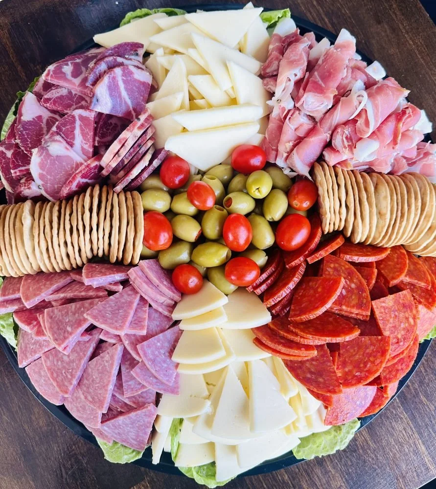 Charcuterie platter with sliced meats, cheeses, cherry tomatoes, green olives, and crackers.