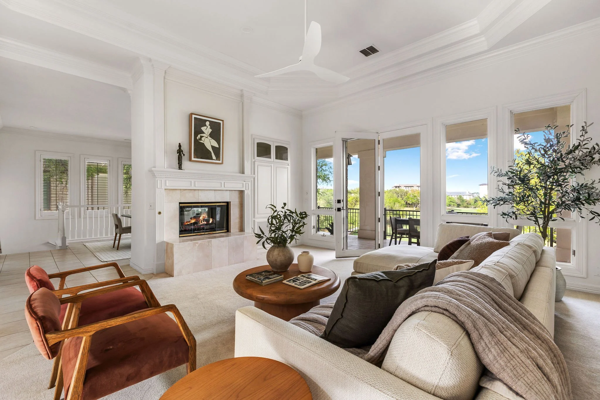 Bright and refined living room at 2305 Barton Creek #25 in The Fairways, featuring a fireplace, beautiful natural light, french doors opening to an expansive deck, and sweeping views of the Fazio Foothills golf course beyond.