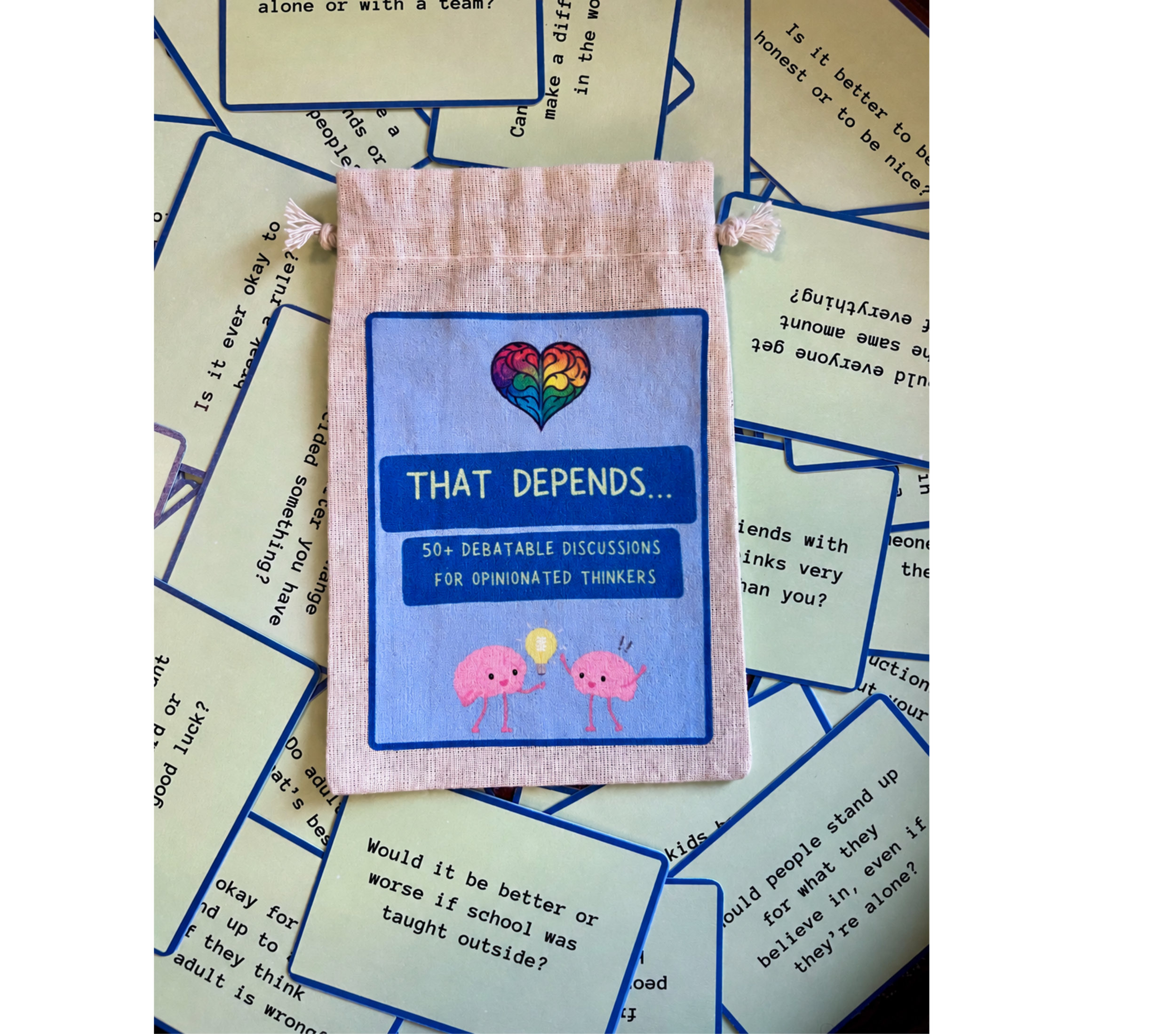 Cards with discussion questions and statements, including a card with a heart and brain illustration and the text "What depends..." with a pink animal illustration at the bottom. The background surface is scattered with similar question cards.