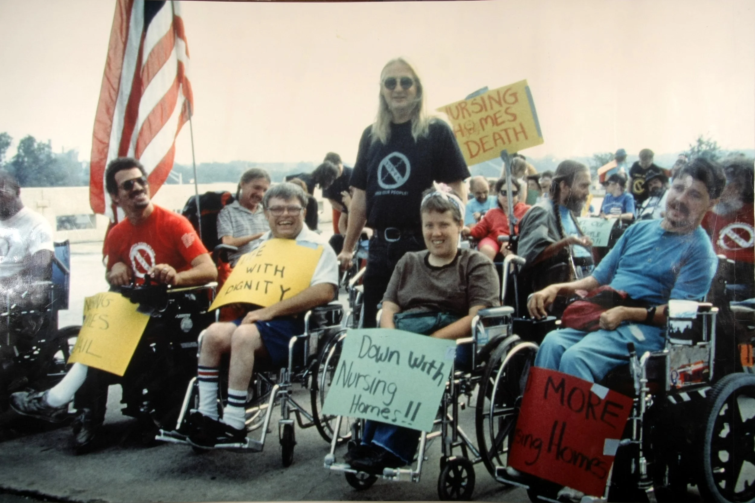 ADAPT demonstrators, most of them wheelchair users, hold hand-lettered signs reading Nursing homes = death and Down with nursing homes