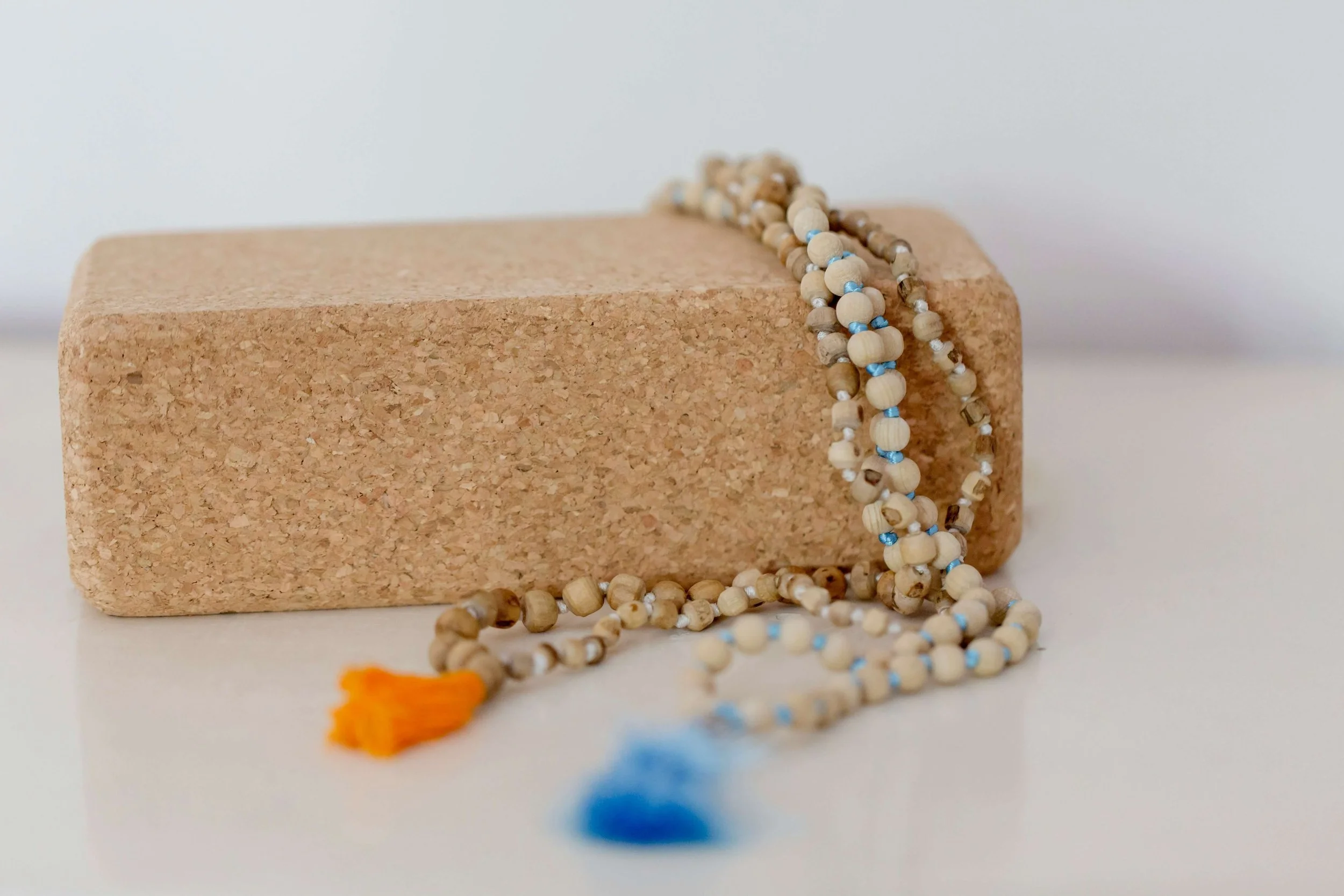 A strand of wooden prayer beads with a blue string, draped over a rectangular cork block on a white surface against a plain white background.