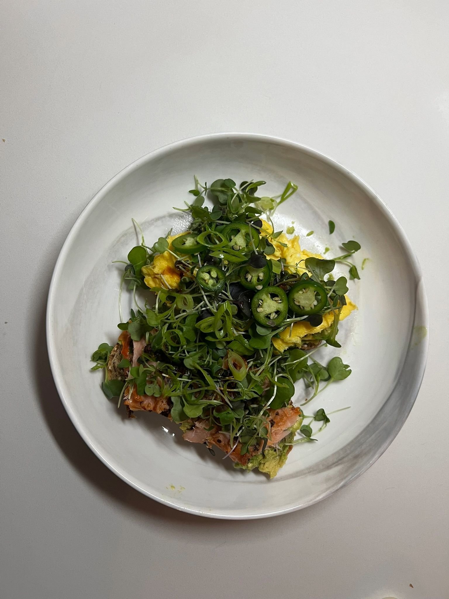 A white oval plate with scrambled eggs topped with microgreens and sliced jalapeños on a white background.