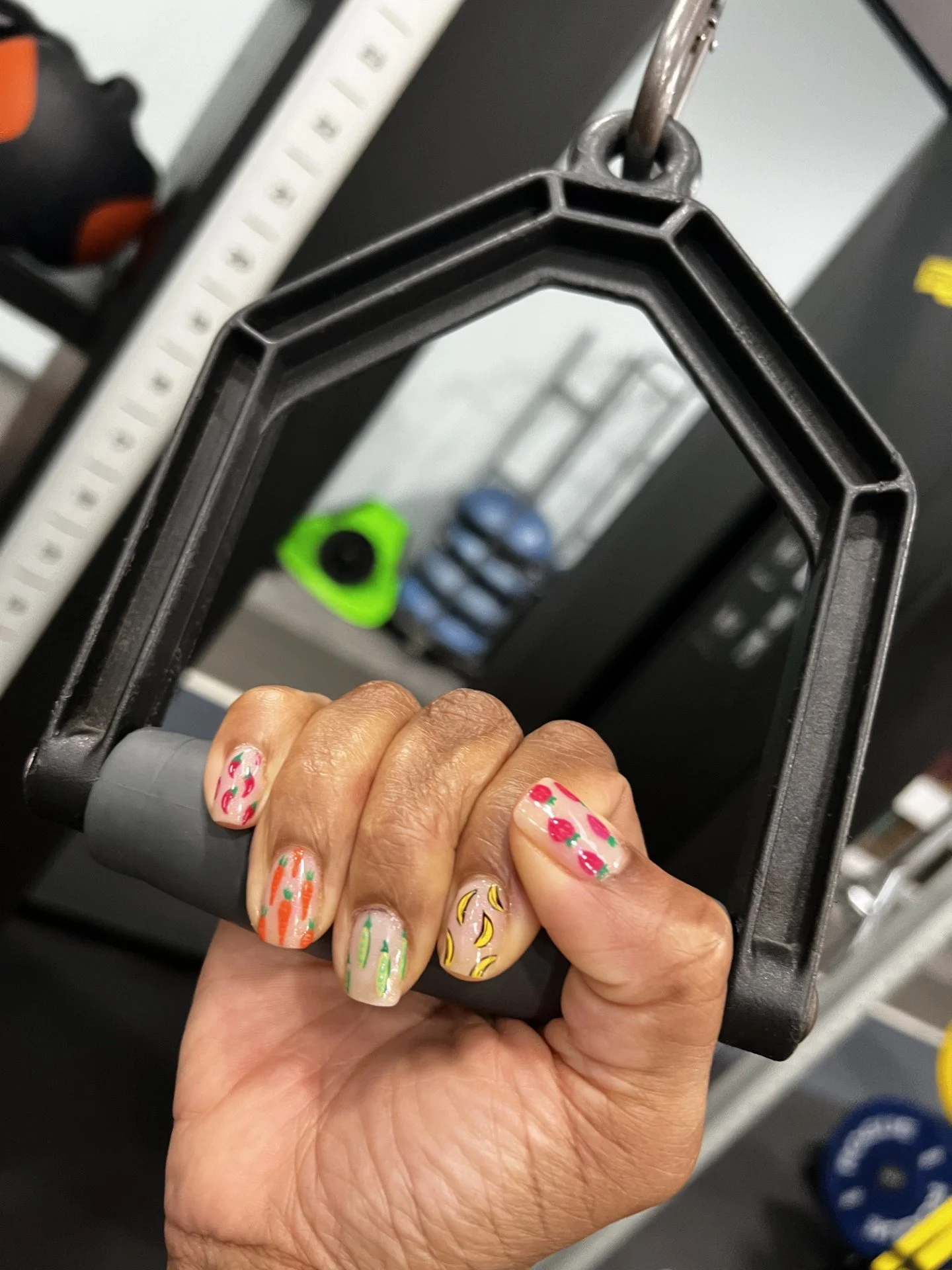 Close-up of a hand holding a black and gray handle of a weightlifting machine, with colorful painted nails featuring floral and abstract designs.