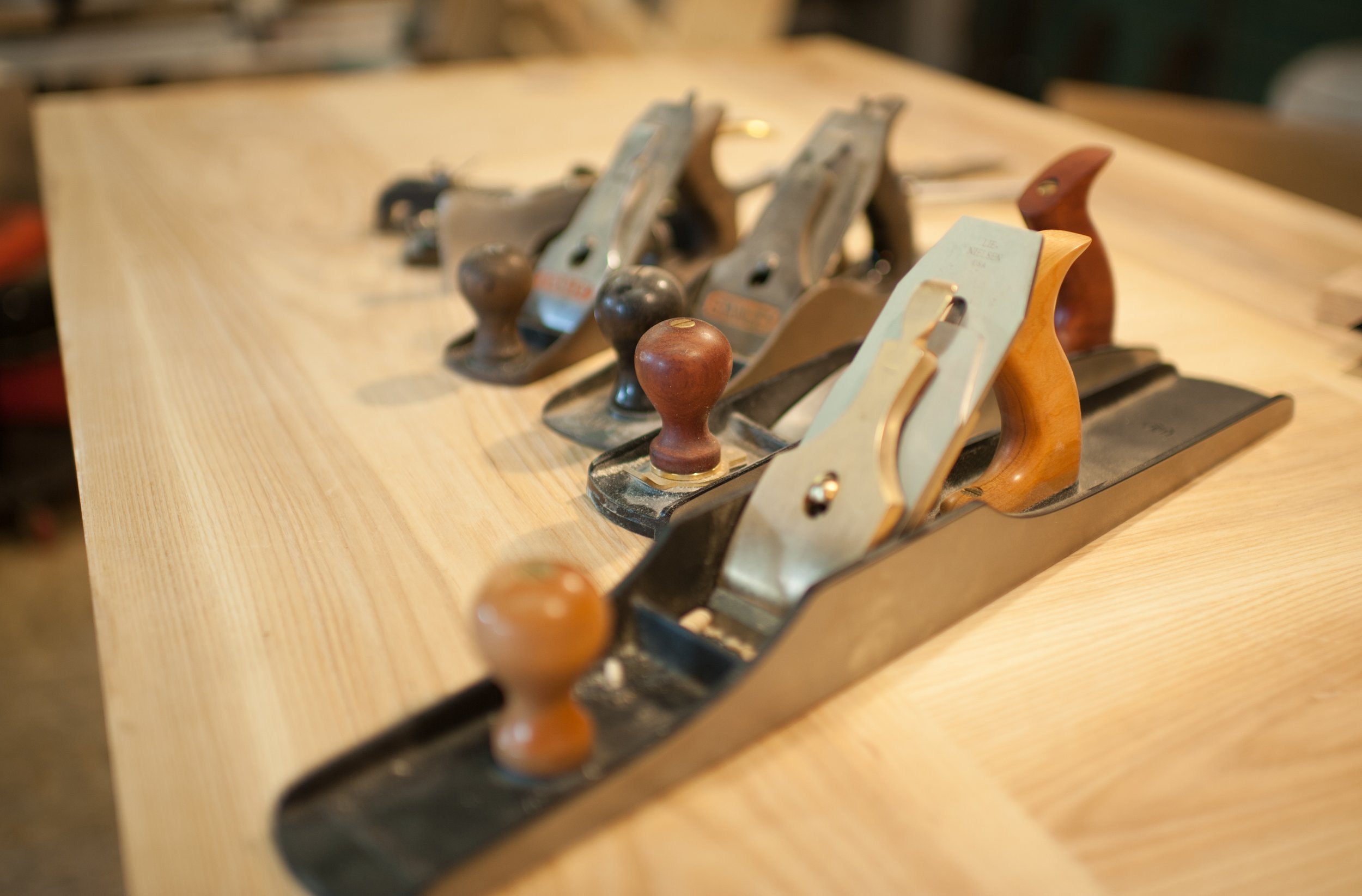 A row of vintage hand planes used for woodworking, arranged on a wooden workbench.
