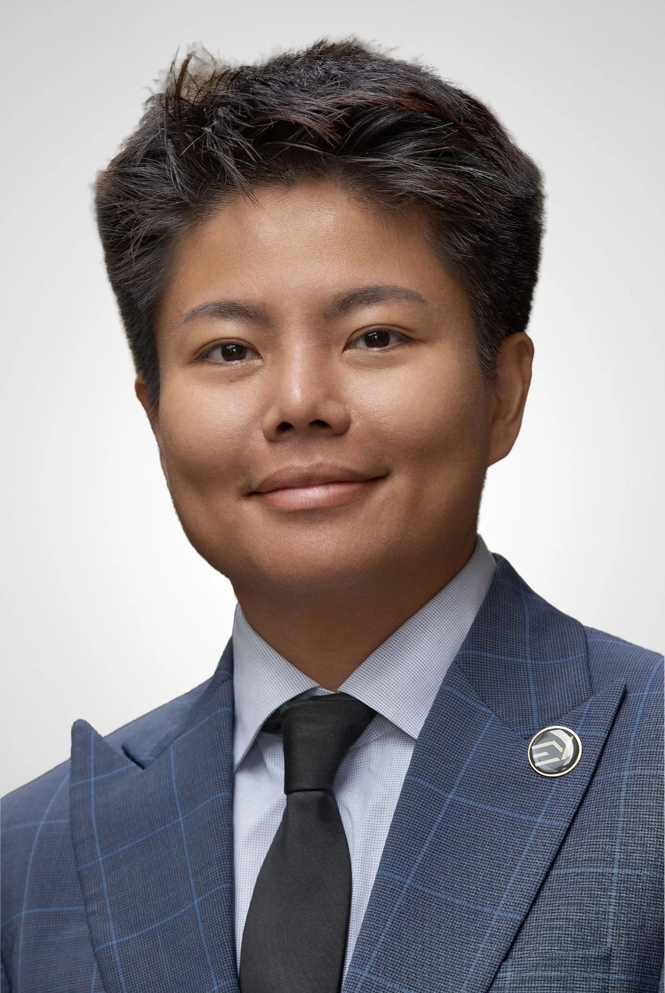Headshot of a man in a blue plaid suit and black tie, smiling, with a white background.