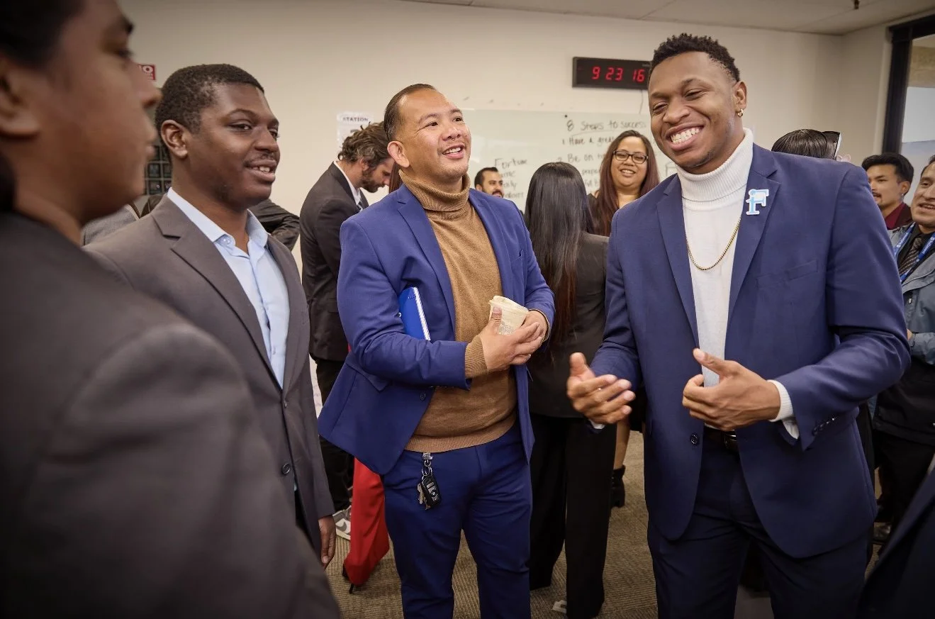 Group of ethnically diverse people in business attire engaging and smiling during a professional gathering or meeting in an office.