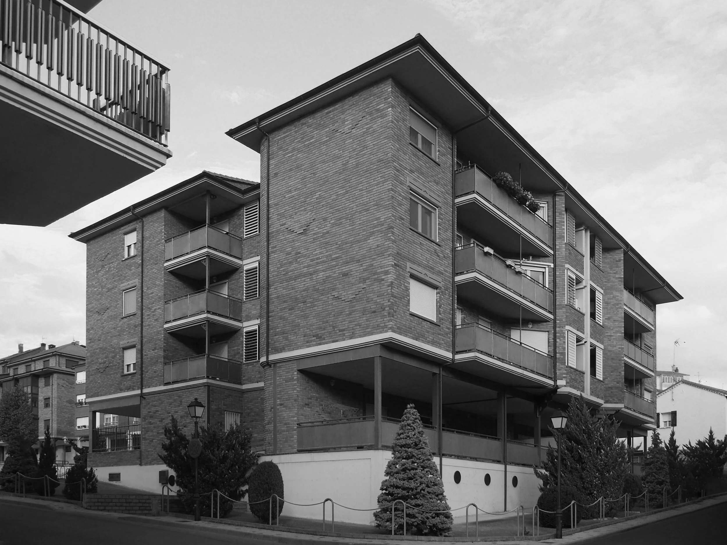 Edificio de apartamentos de ladrillo con múltiples balcones y ventanas en un entorno urbano, en blanco y negro.