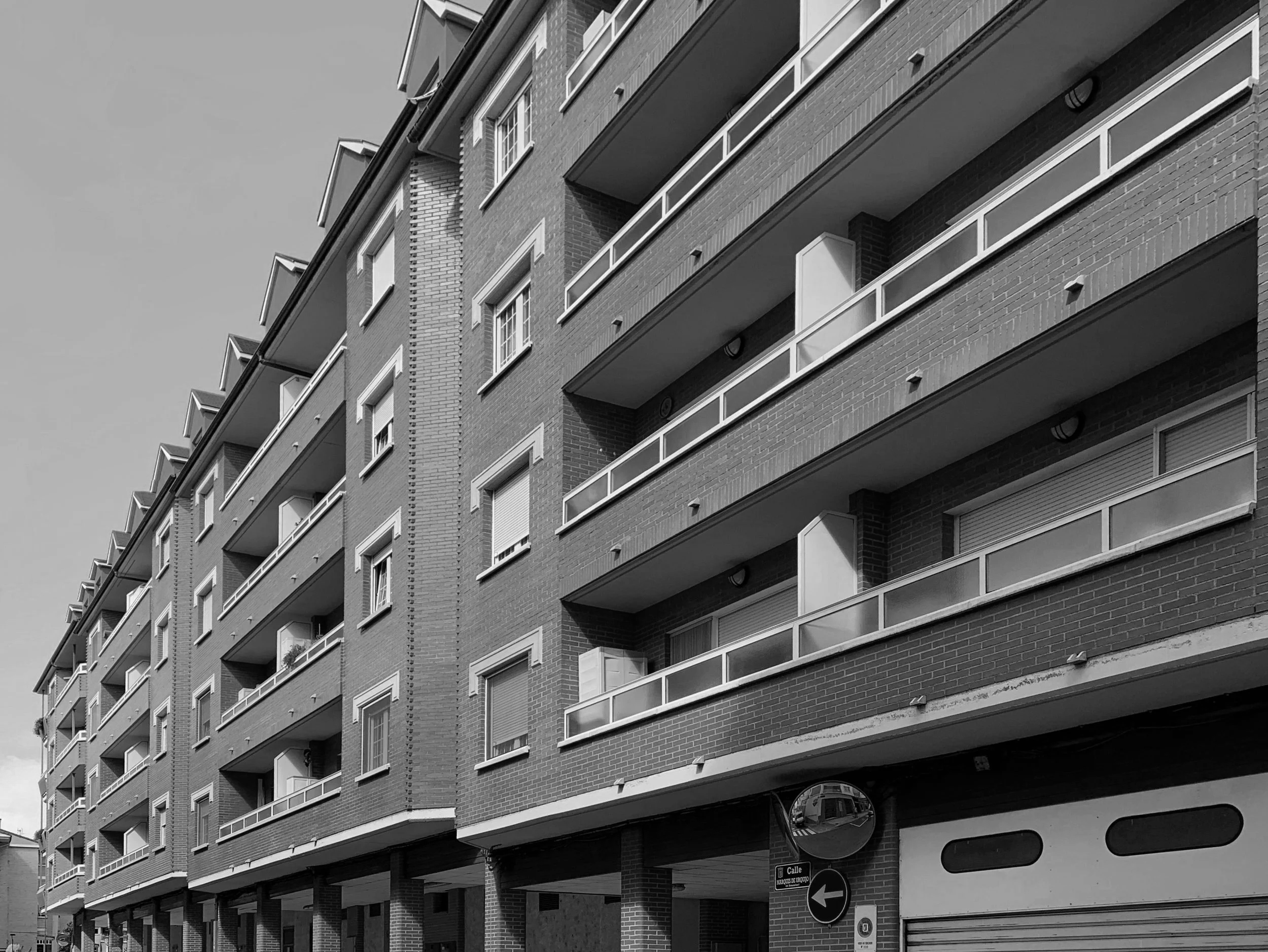Vista de un edificio de departamentos de varios pisos, con balcones y ventanas rectangulares, en una imagen en blanco y negro.