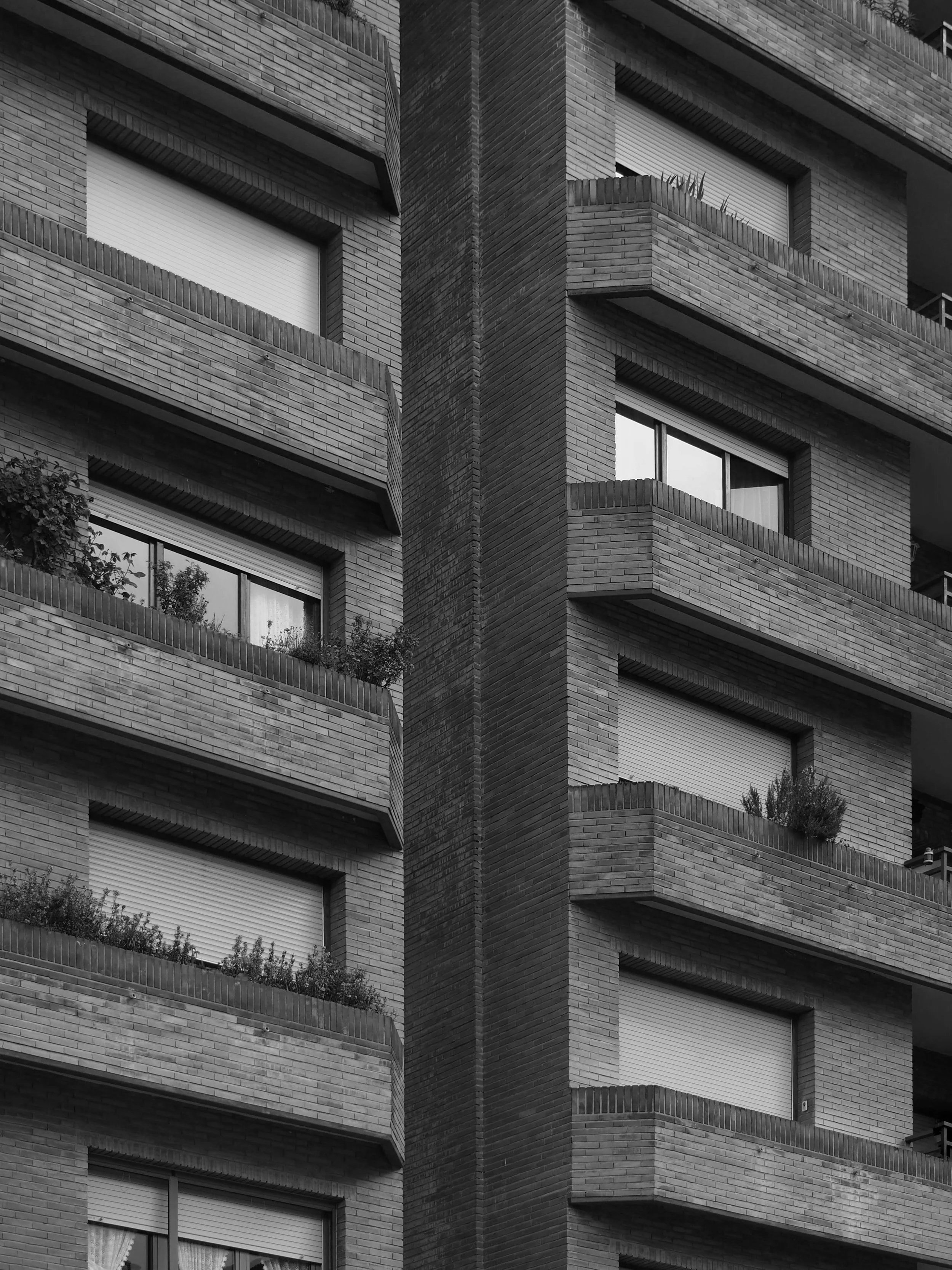 Edificio de apartamentos de ladrillo con ventanas y terrazas con plantas.