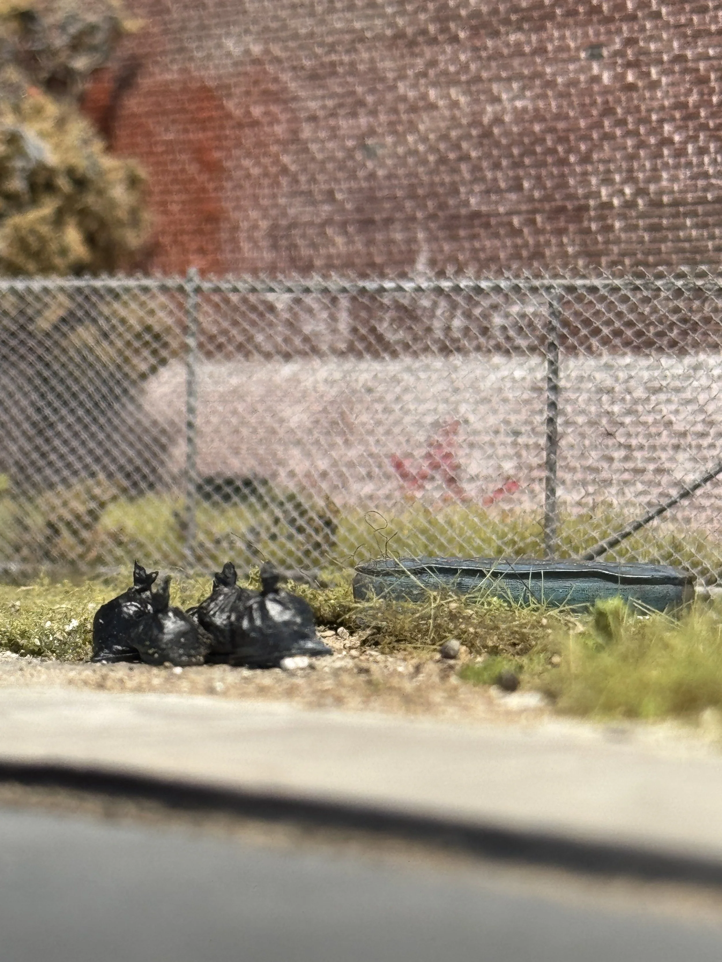 View through a window screen showing a pile of burnt objects, grass, and a brick wall in the background.