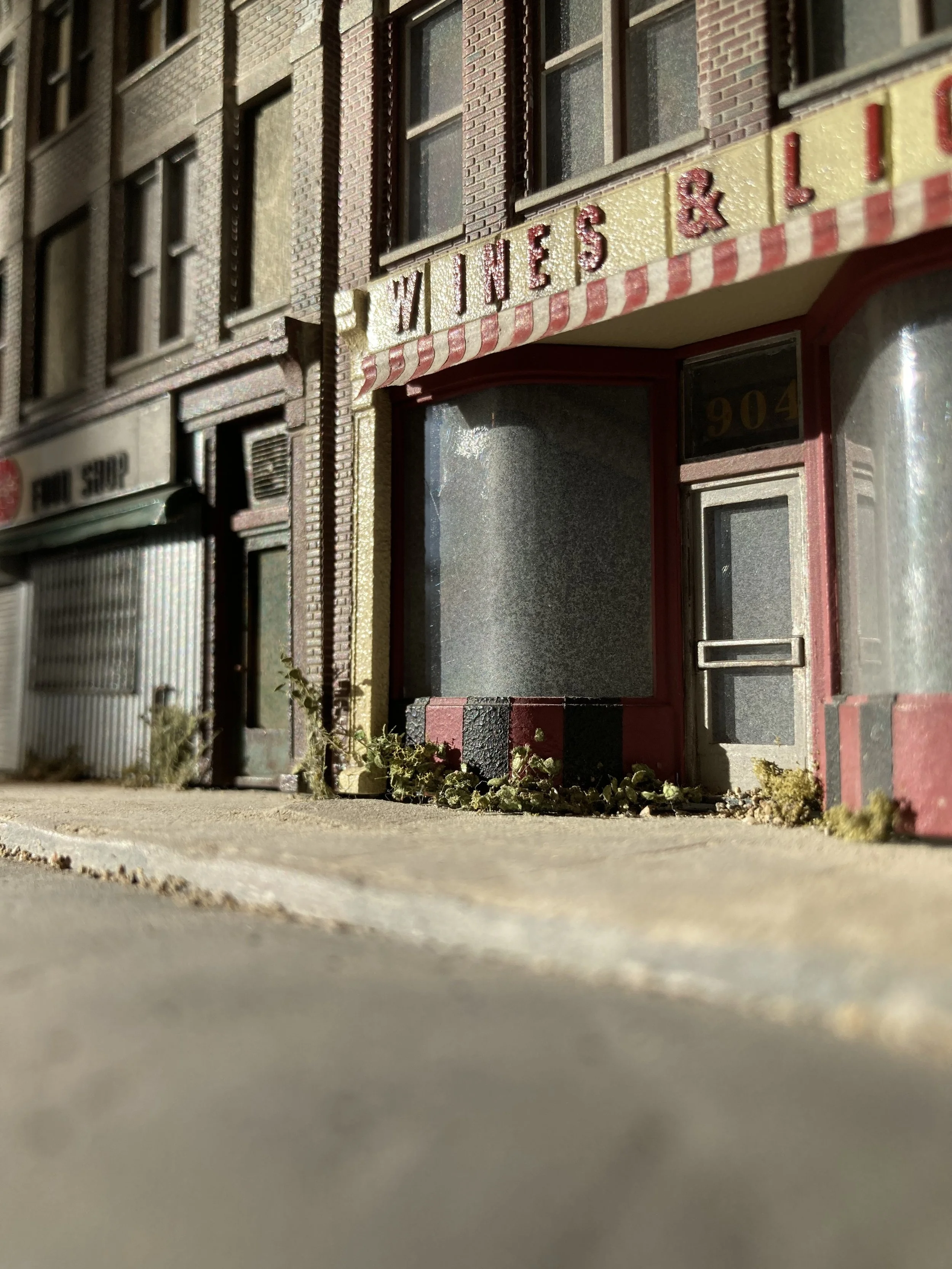 Close-up of a miniature building facade with sign reading 'WILES & L', showing brick details, windows, and a door, taken from ground level.
