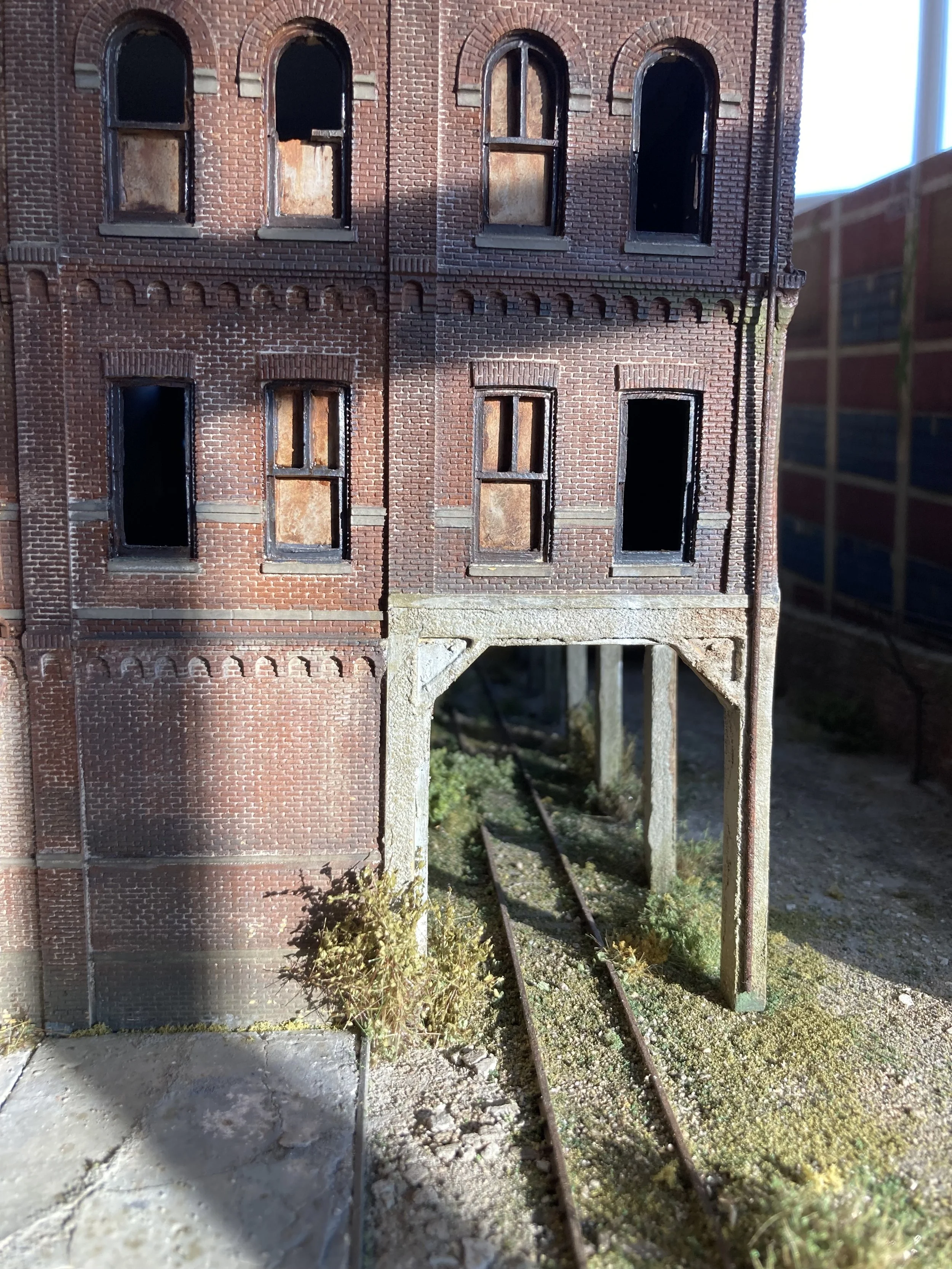 A detailed model of an old brick building with broken windows and an elevated train track underneath.