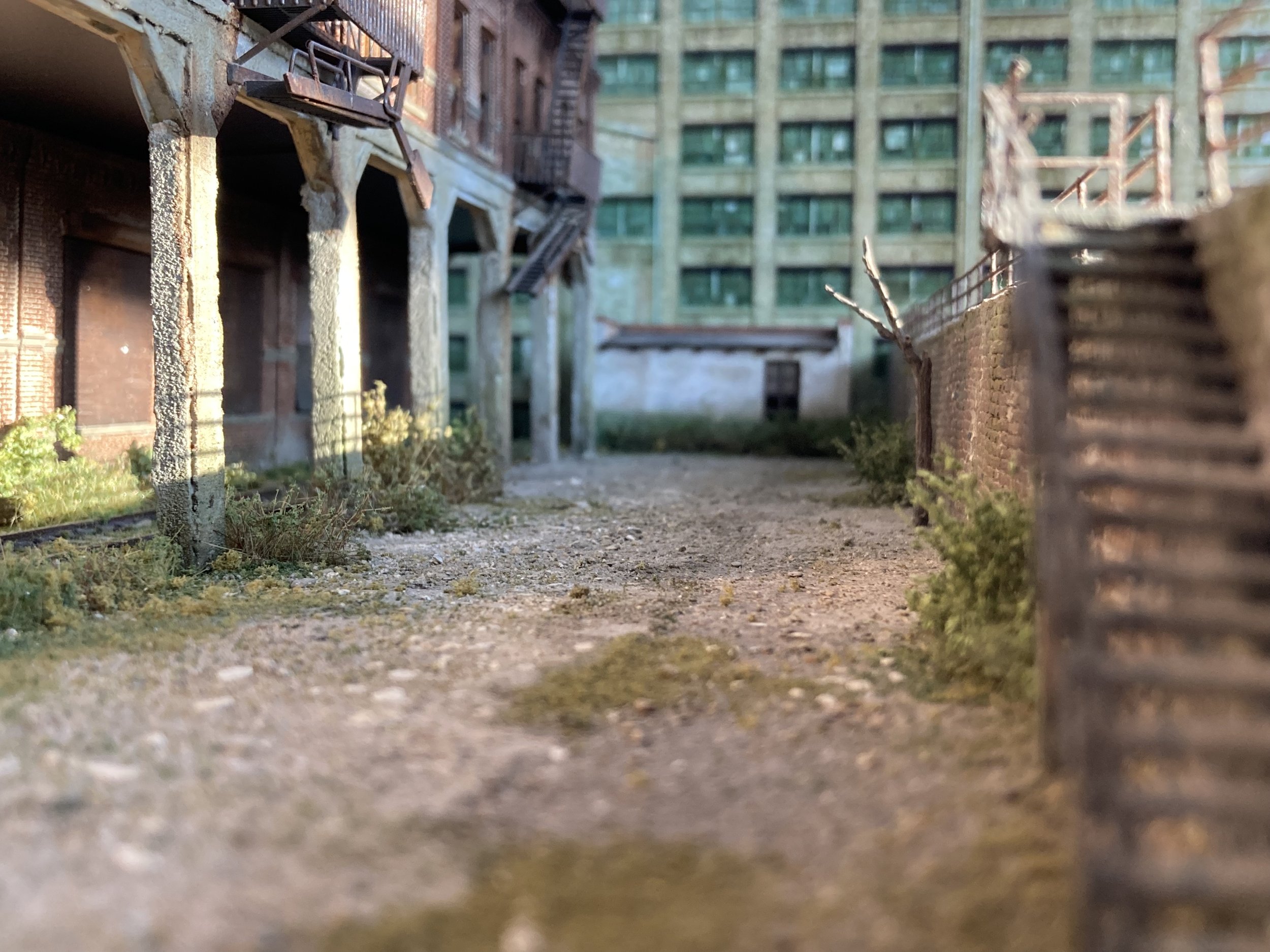 Close-up of a miniature alleyway with detailed buildings, brick walls, fire escapes, and barbed wire fence, creating a realistic cityscape scene.