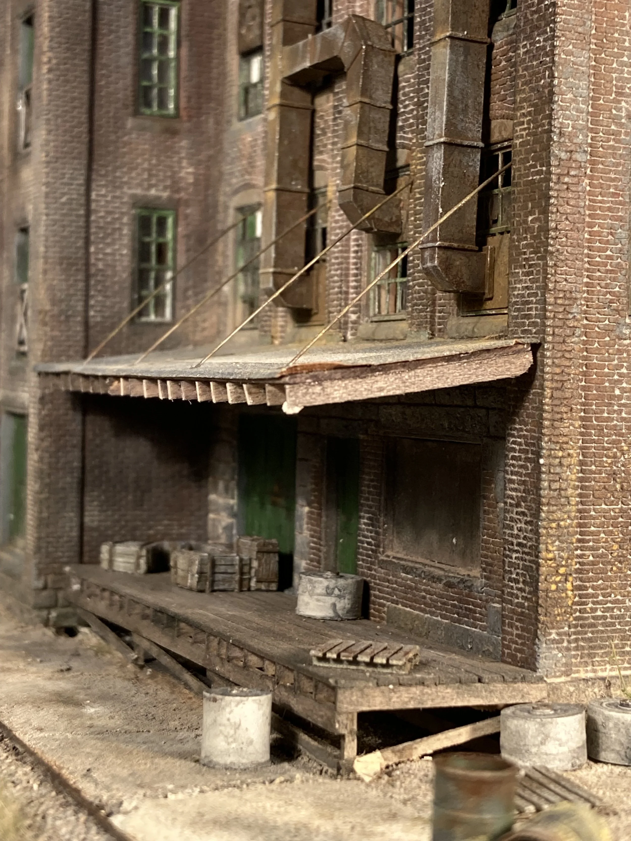Close-up of a model building made of brick with small windows, a wooden platform, and various construction materials in the foreground.