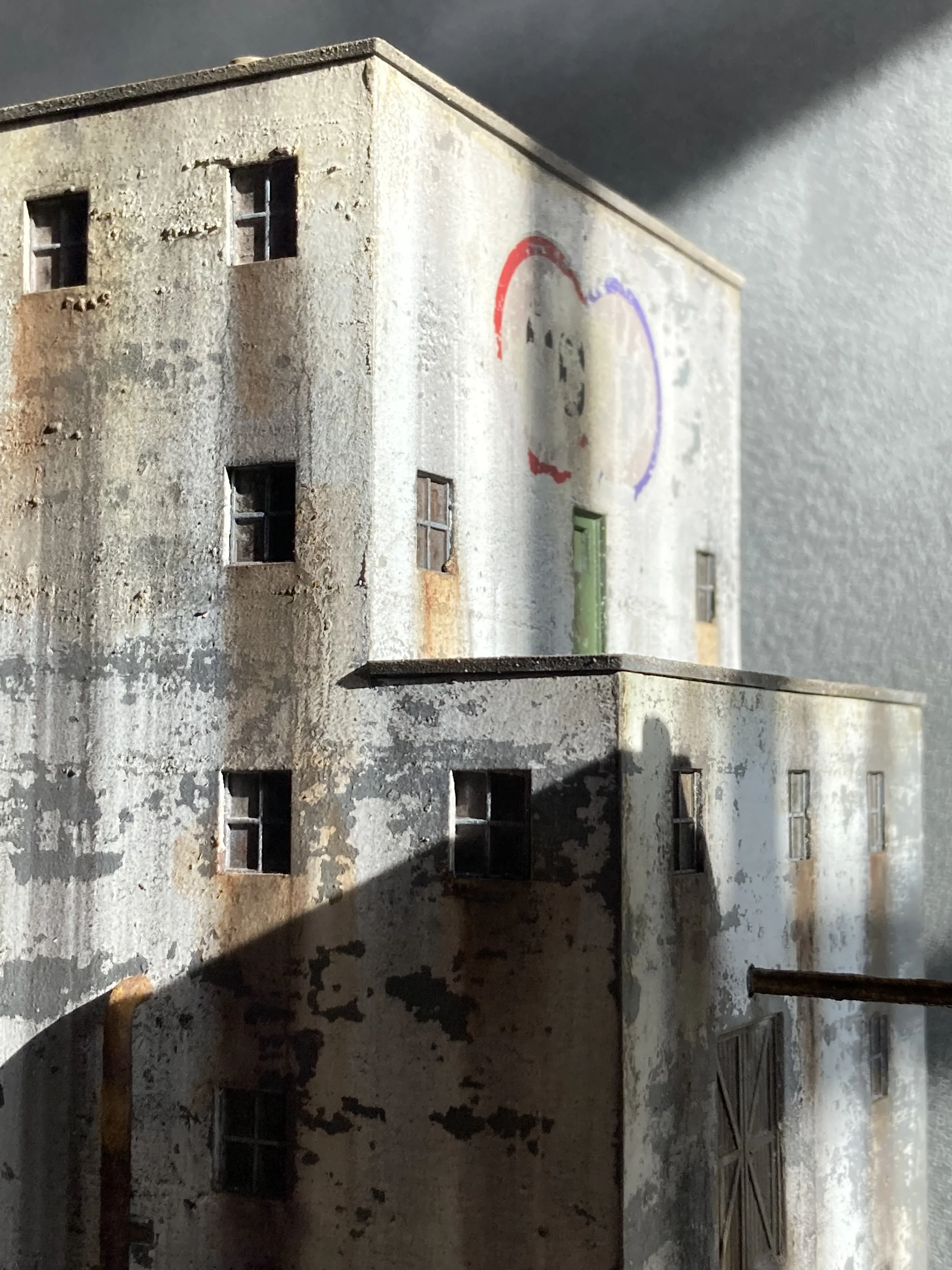 Close-up of an old, weathered building with peeling paint, small windows, and a graffiti heart mural on the wall.