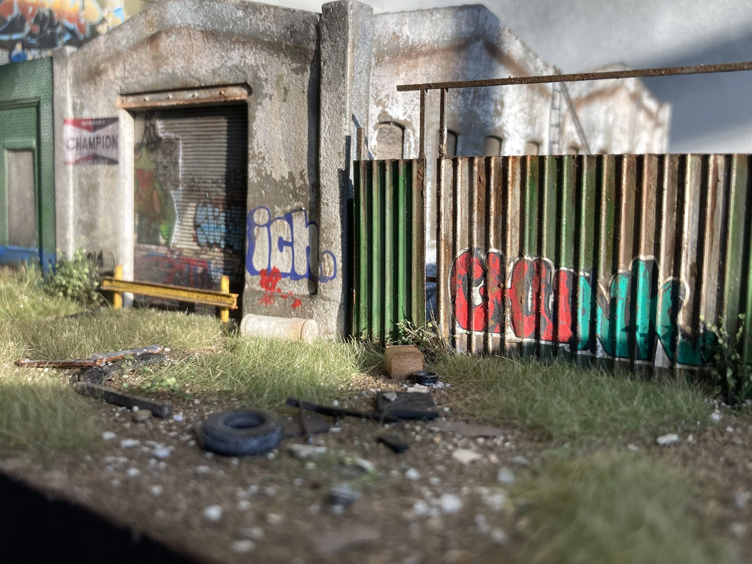 Close-up of a weathered building exterior with graffiti, rusty gate, and scattered debris on the ground, including small tires.