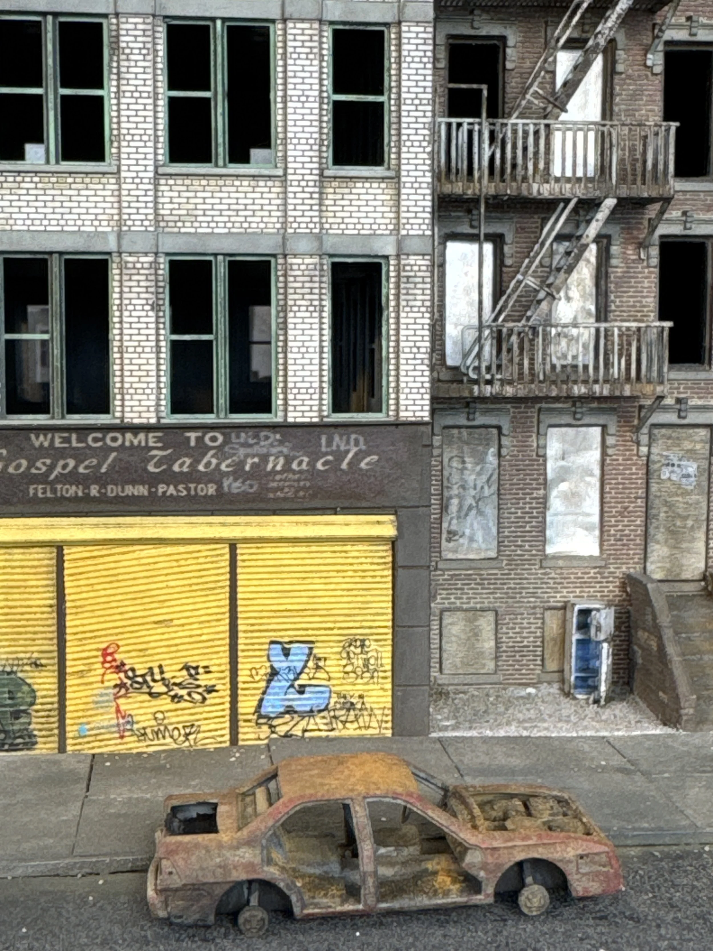 Flooded, rusted car in front of brick buildings with boarded-up windows, graffiti-covered yellow storefront with closed shutters.