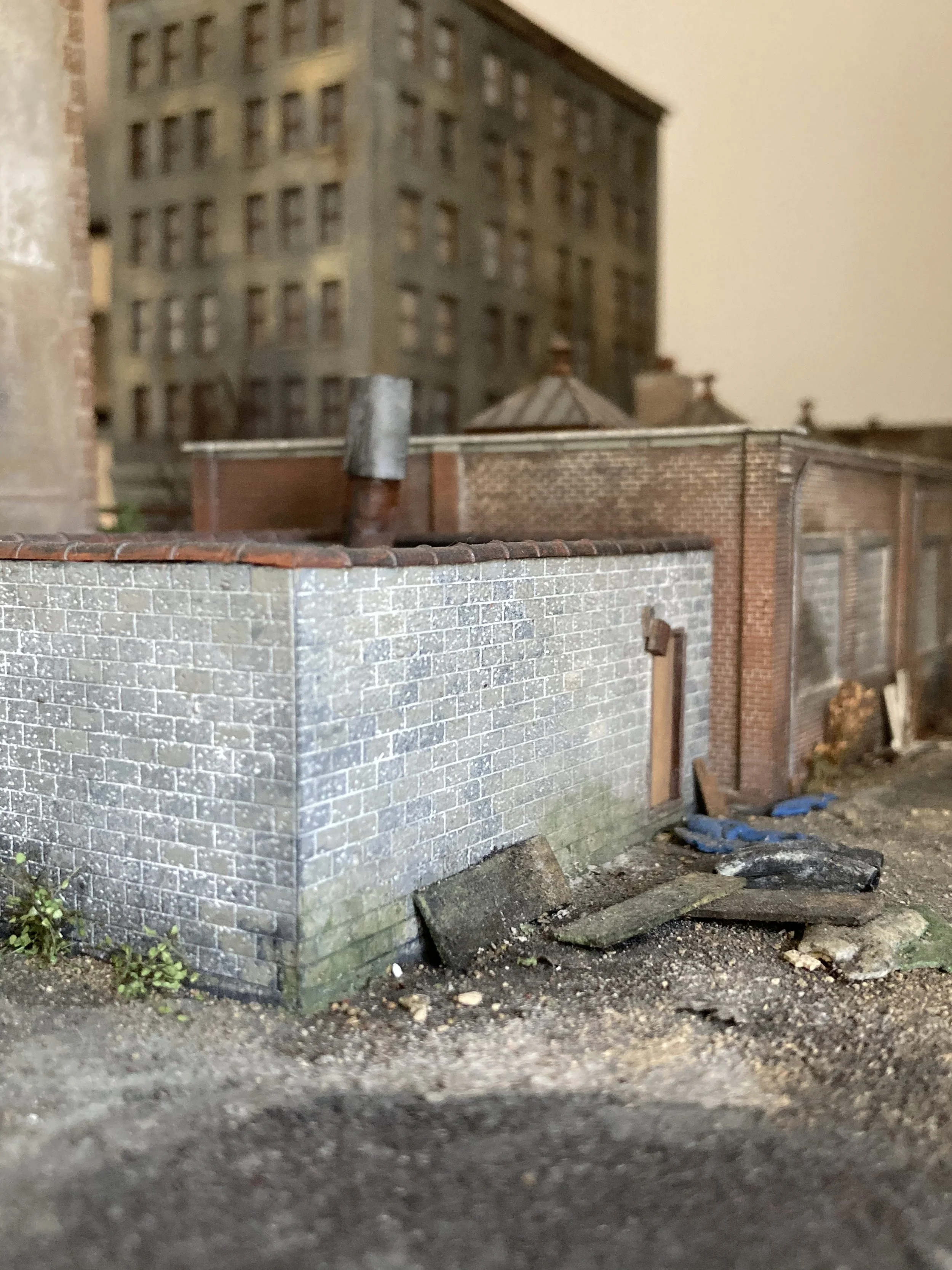 Close-up of a miniature building model with brick and stone walls, with debris and dirt on the ground in the foreground.