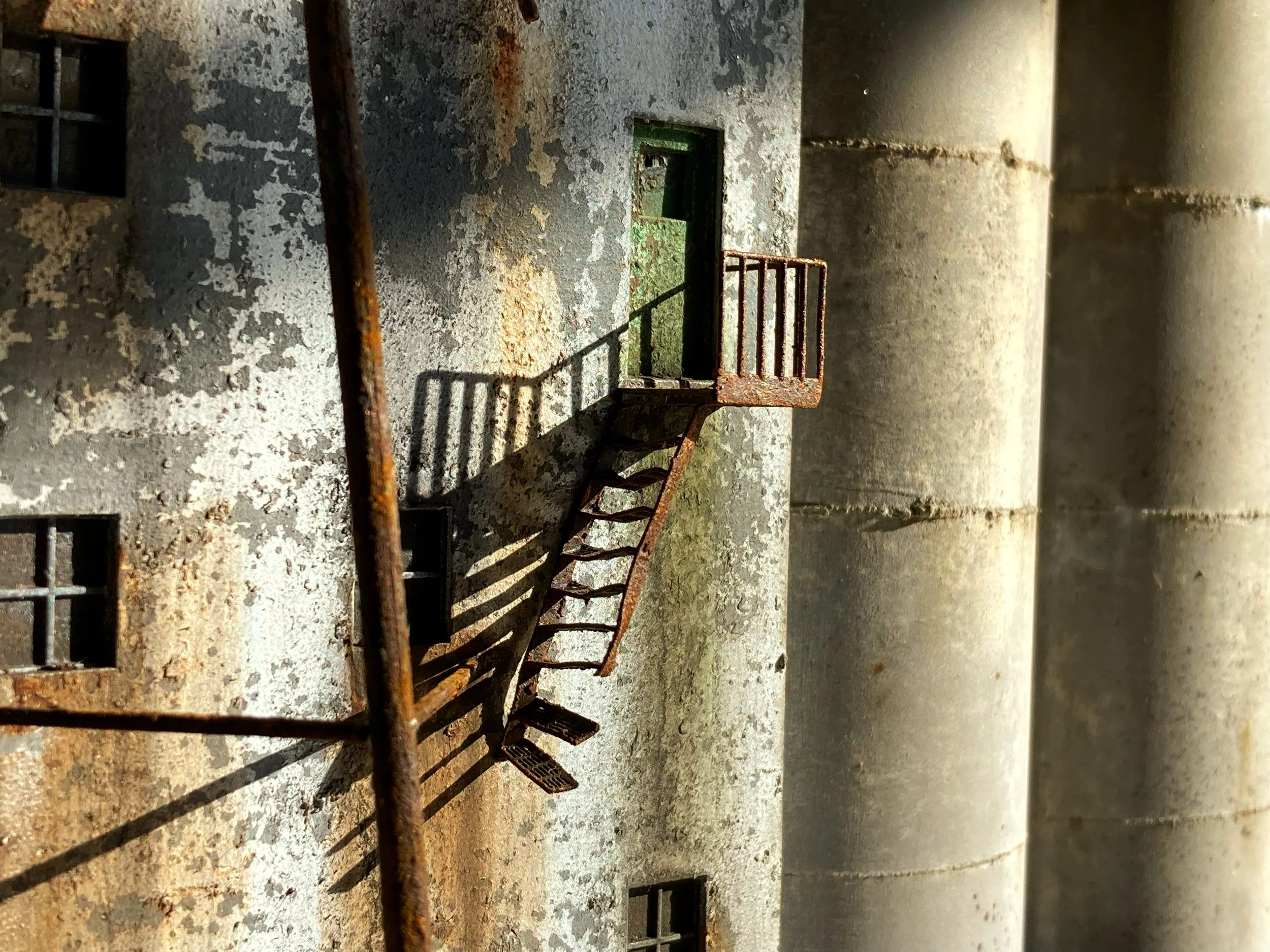 Close-up of a rusty, weathered metal staircase outside a concrete building with weathered walls and small grated windows.