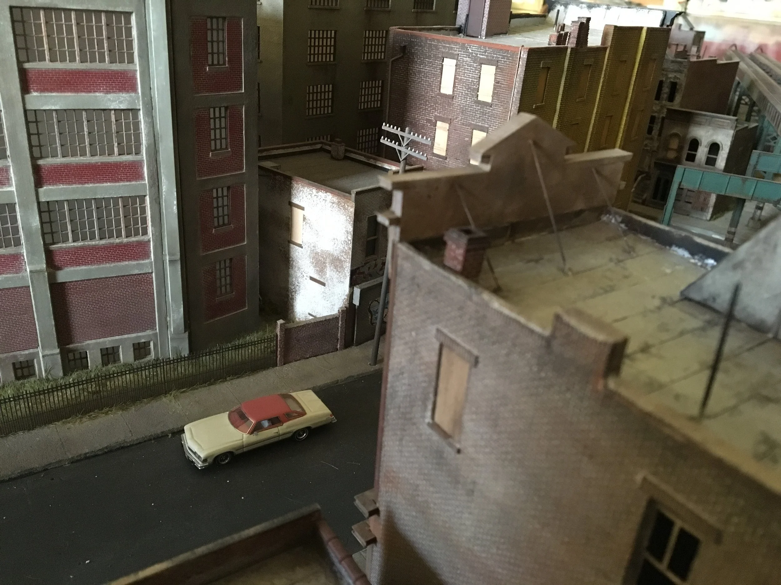 Miniature city scene with detailed buildings, including brick walls, windows, and fire escapes, along with a small yellow car on a street.