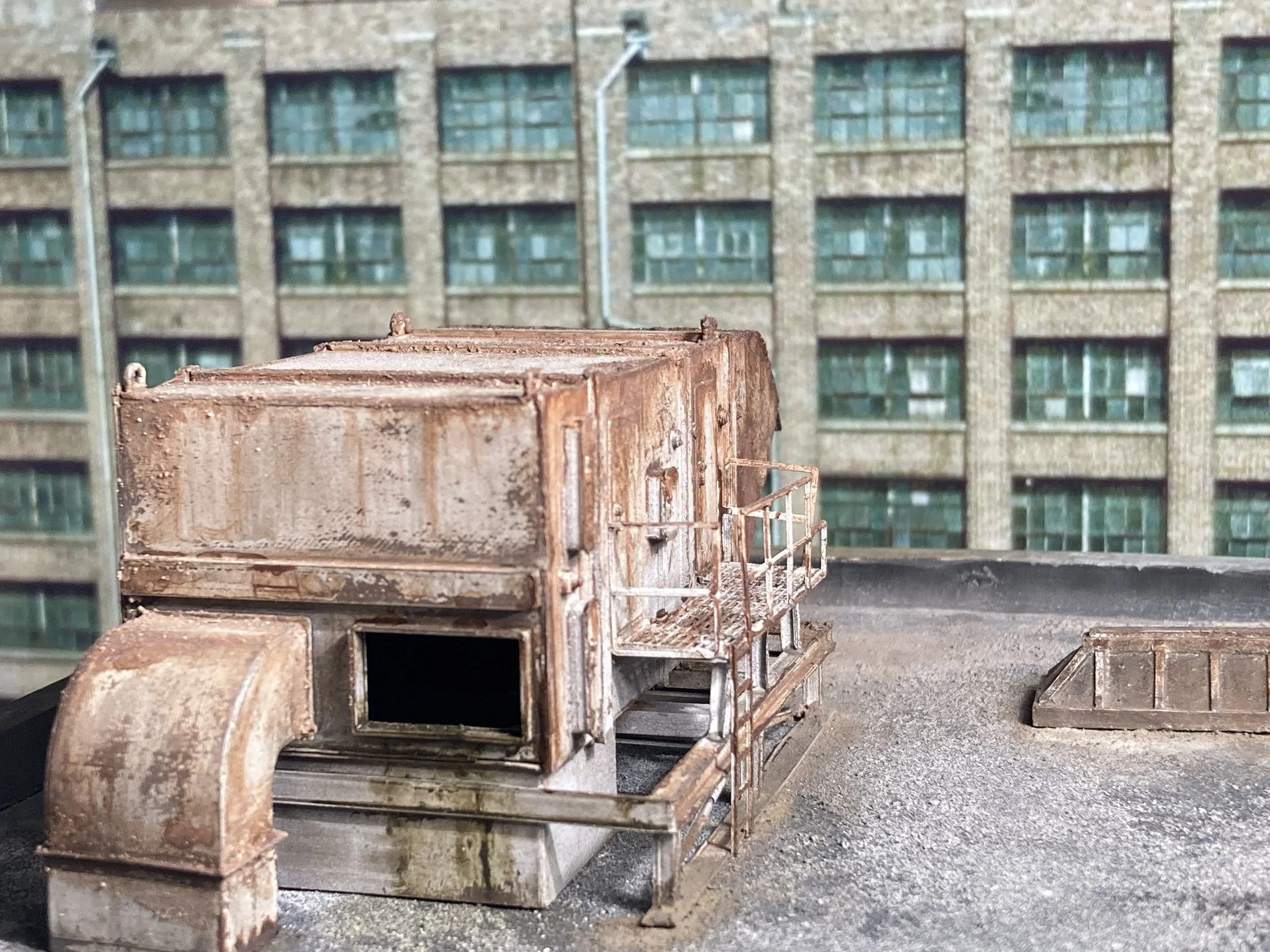Rusty, abandoned metal carts arranged in rows on a concrete surface with a brick building with green windows in the background.