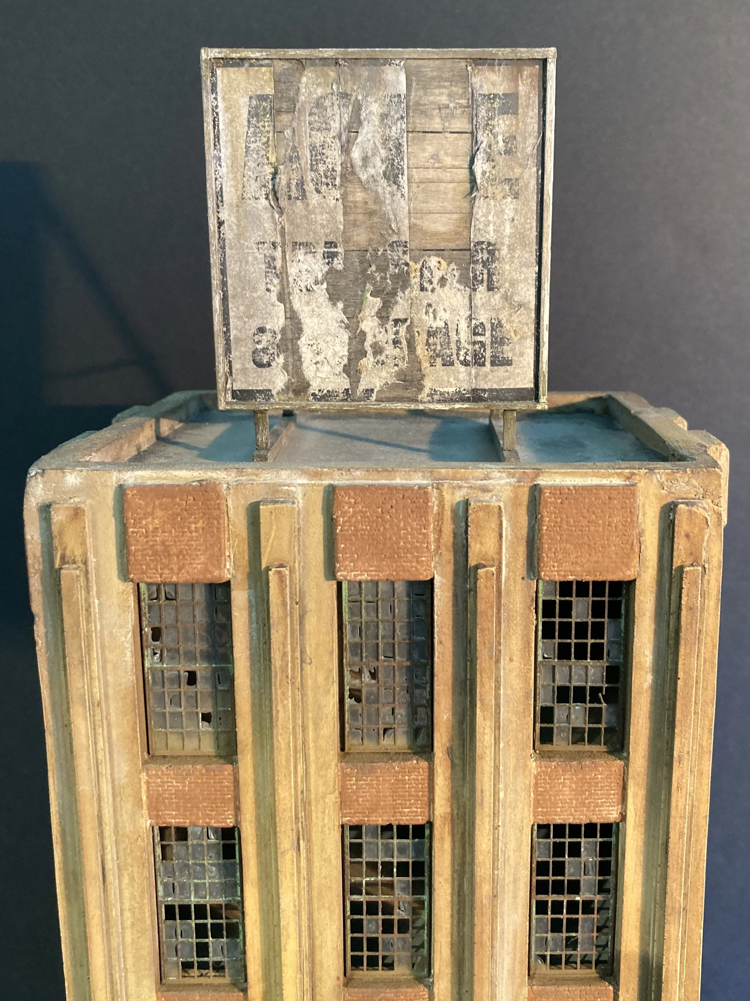 A decorative miniature building resembling a factory or warehouse, made of wood and brick, with multiple small windows and a weathered sign on top.