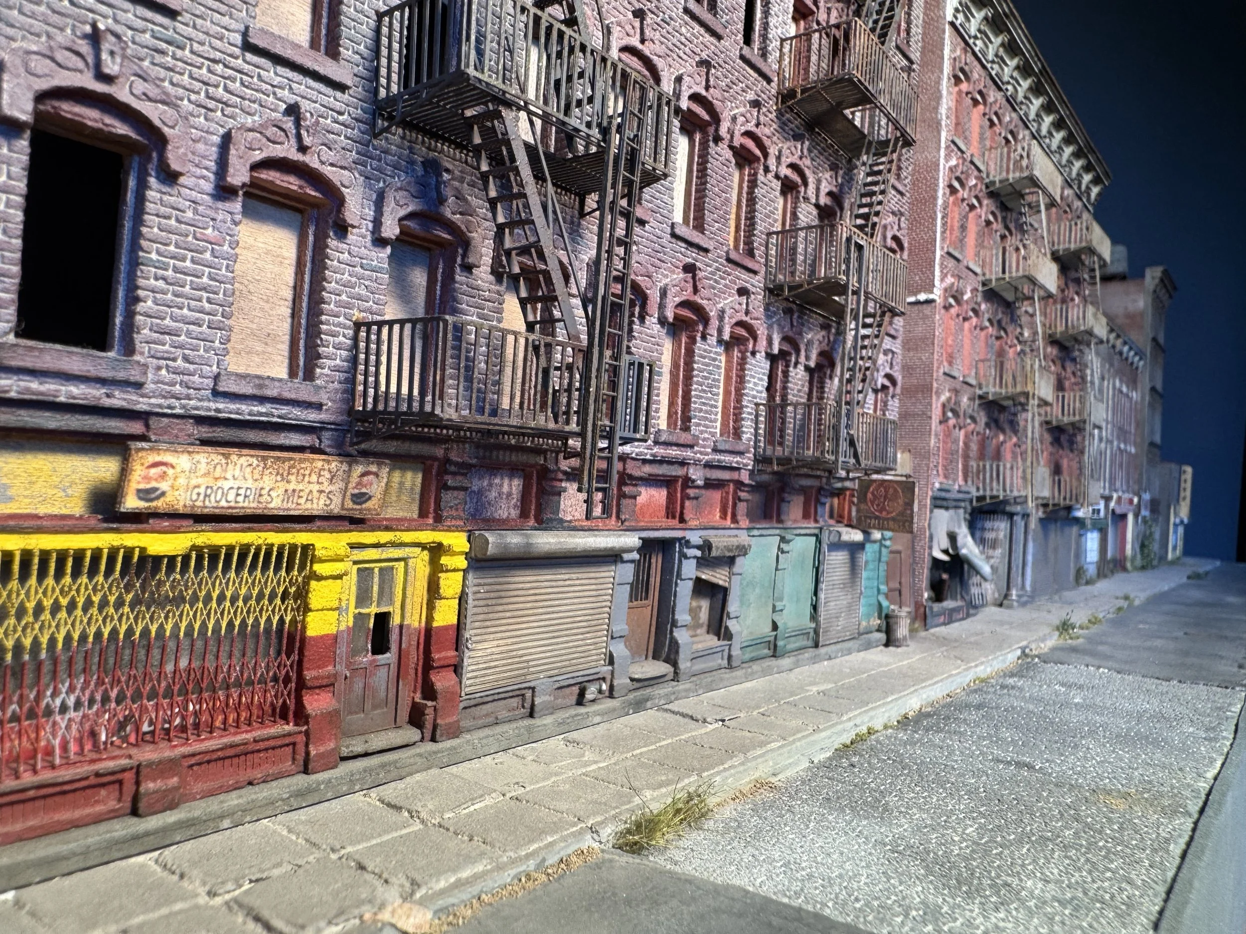 A row of old brick buildings with fire escapes and closed storefronts on a sidewalk, under a dark sky.