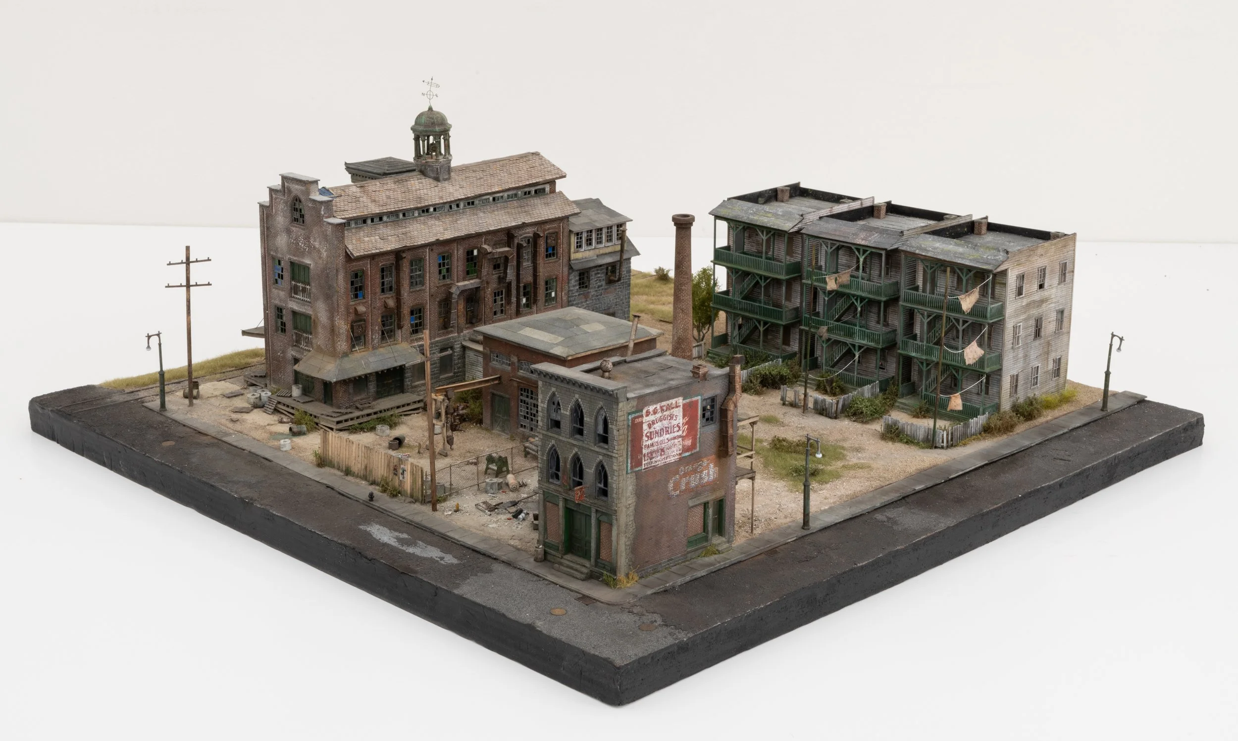 Detailed miniature model of an abandoned urban industrial complex, featuring weathered buildings, debris, and overgrown vegetation.