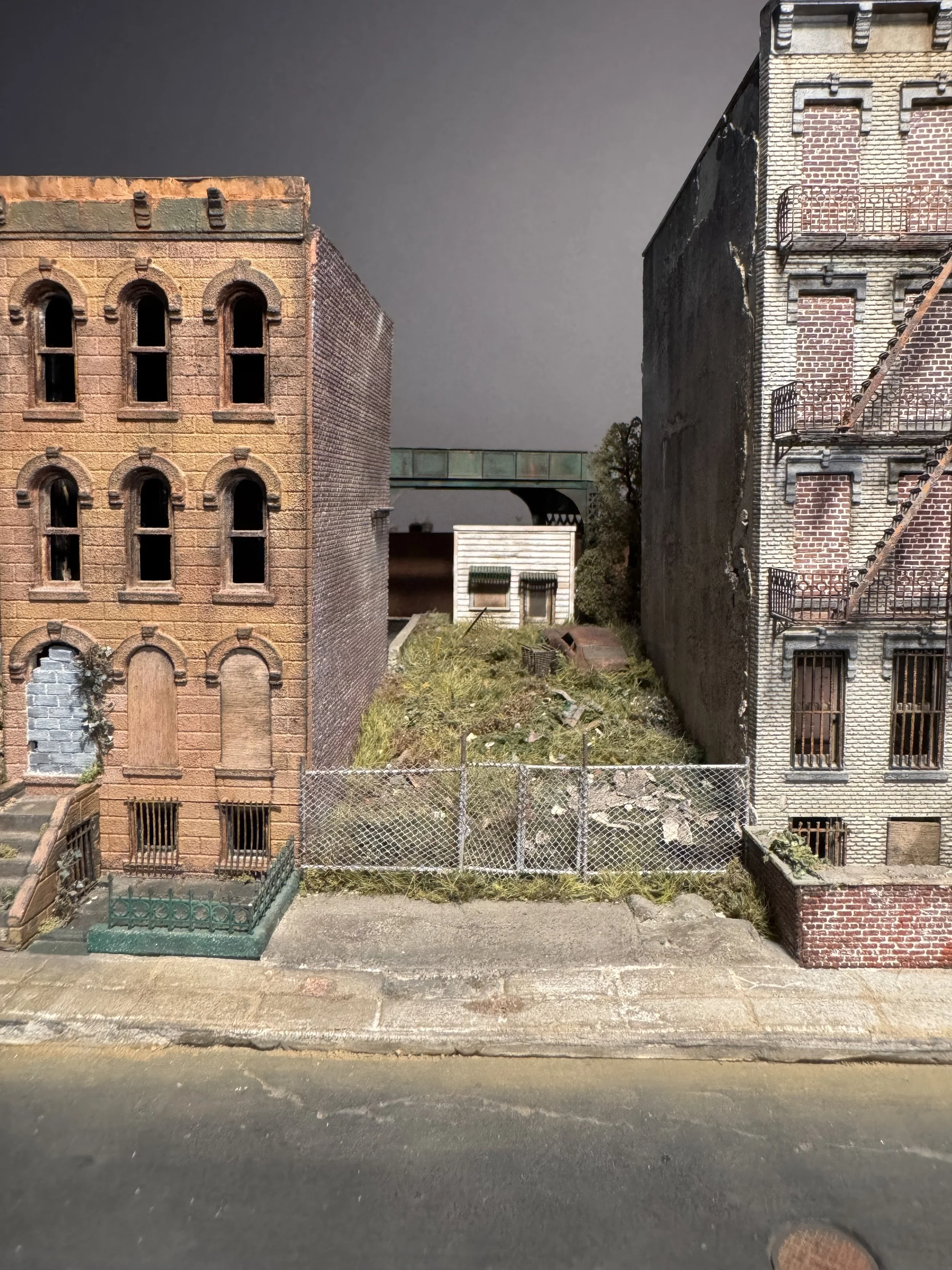 Miniature model of three old brick buildings with a fence and grass in front, viewed from the street.