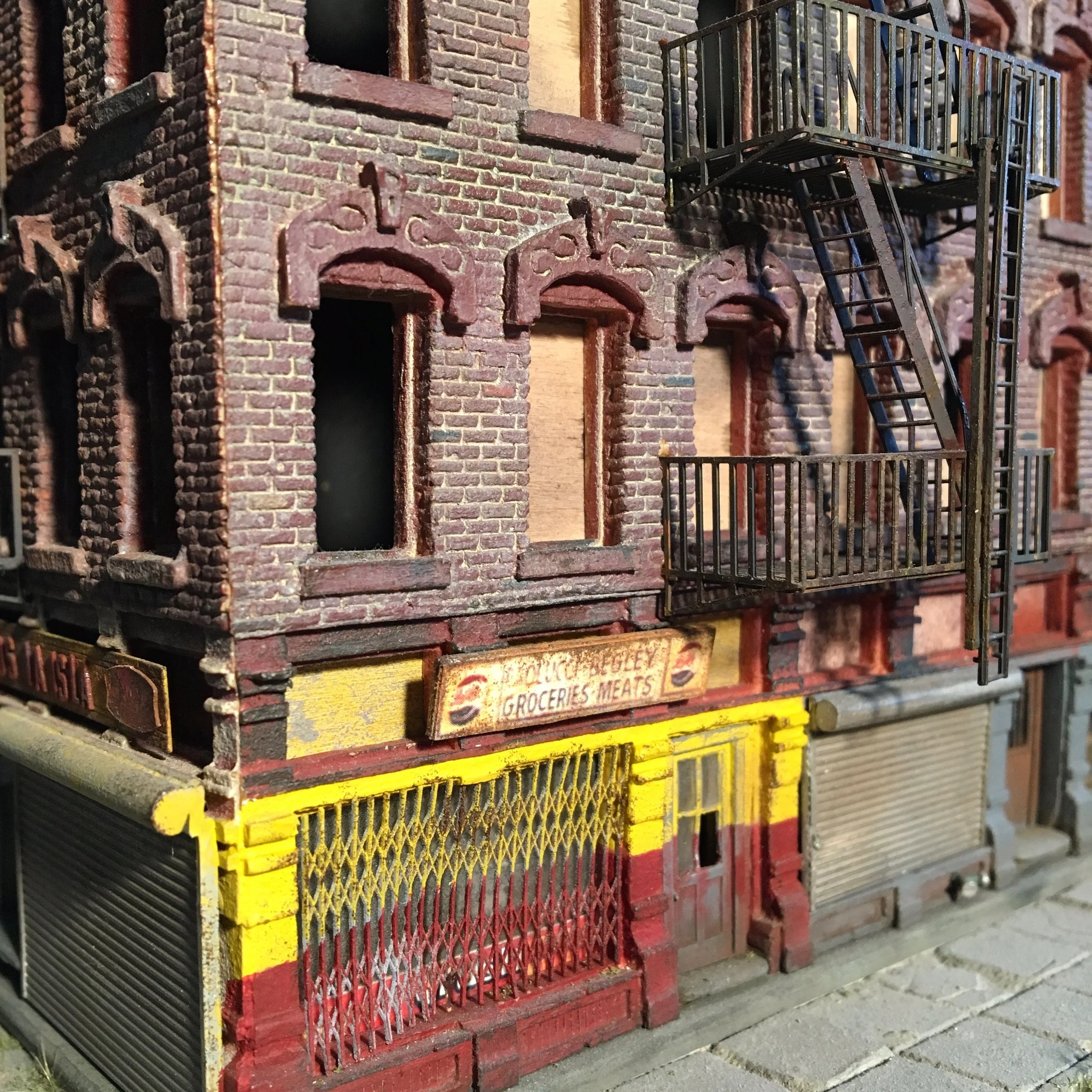 Stack of miniature building models made of brick and metal, resembling small row houses with fire escapes. Some models are painted in bright colors like yellow and red.