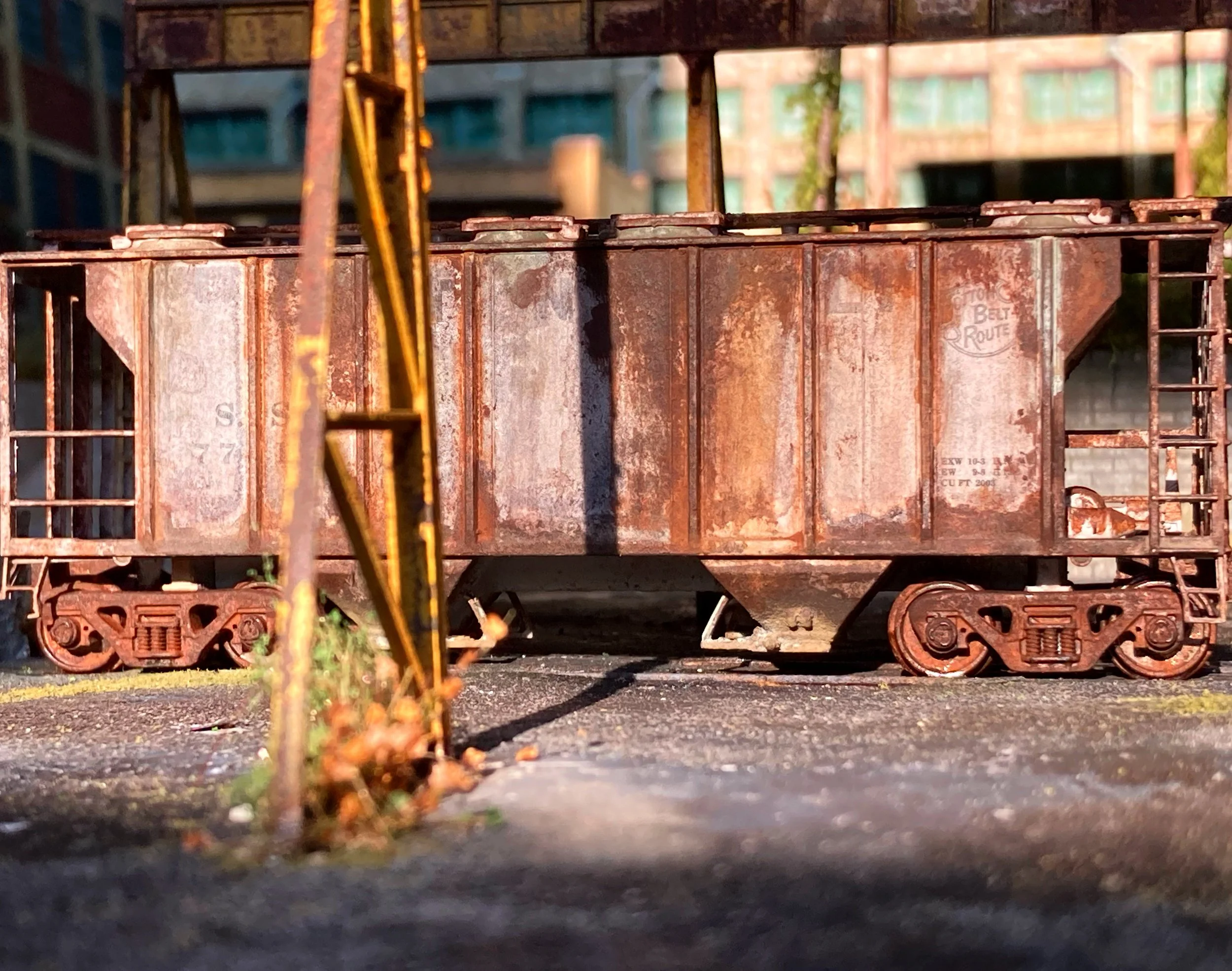 A rusty model train car on a model railway track with a brick building in the background.