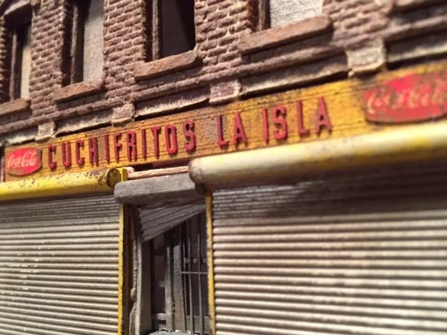 Closed storefront with a brick building above and a sign that reads 'Cuchifritos La Isla' in red letters.