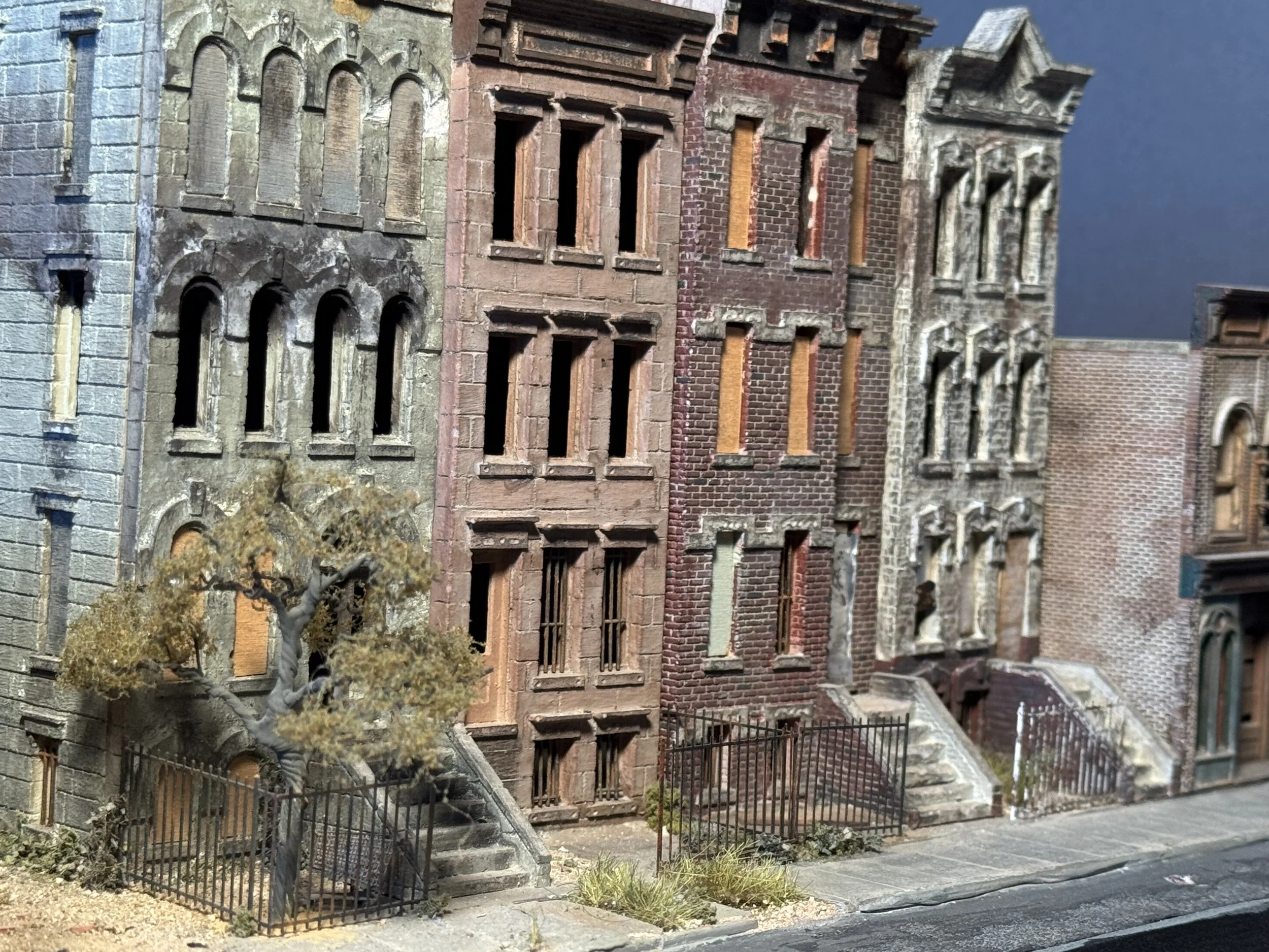 A miniature model of old brick and stone buildings with detailed windows, stairs, and fencing in front.