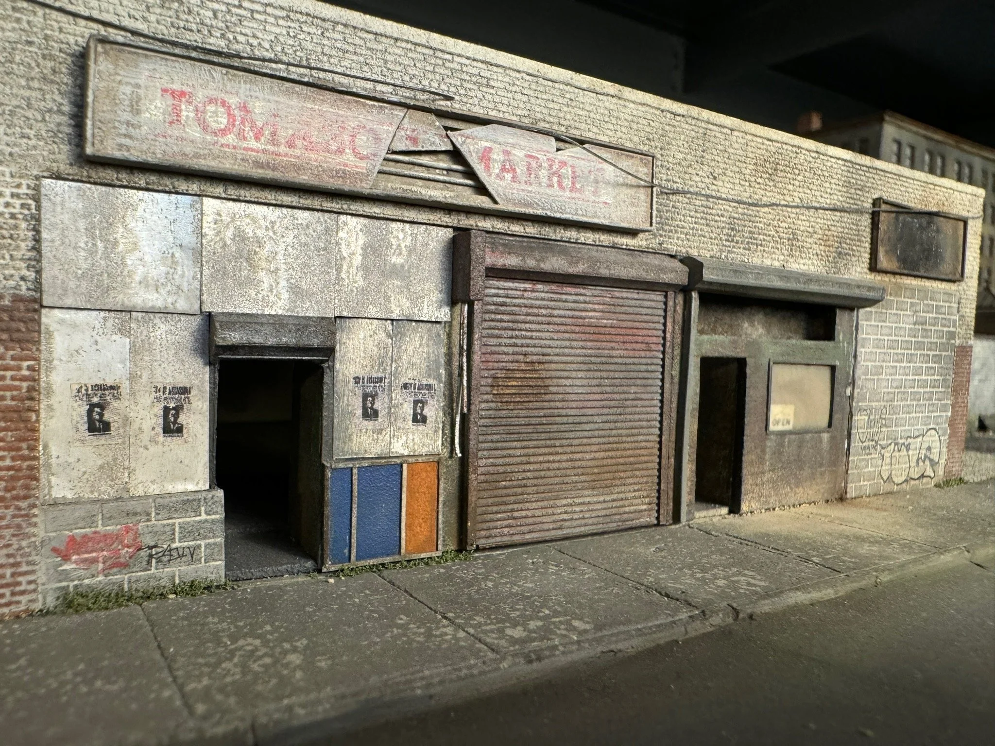 A row of boarded-up storefronts with rusted metal shutter doors, graffiti on the walls, and a sidewalk in the foreground.