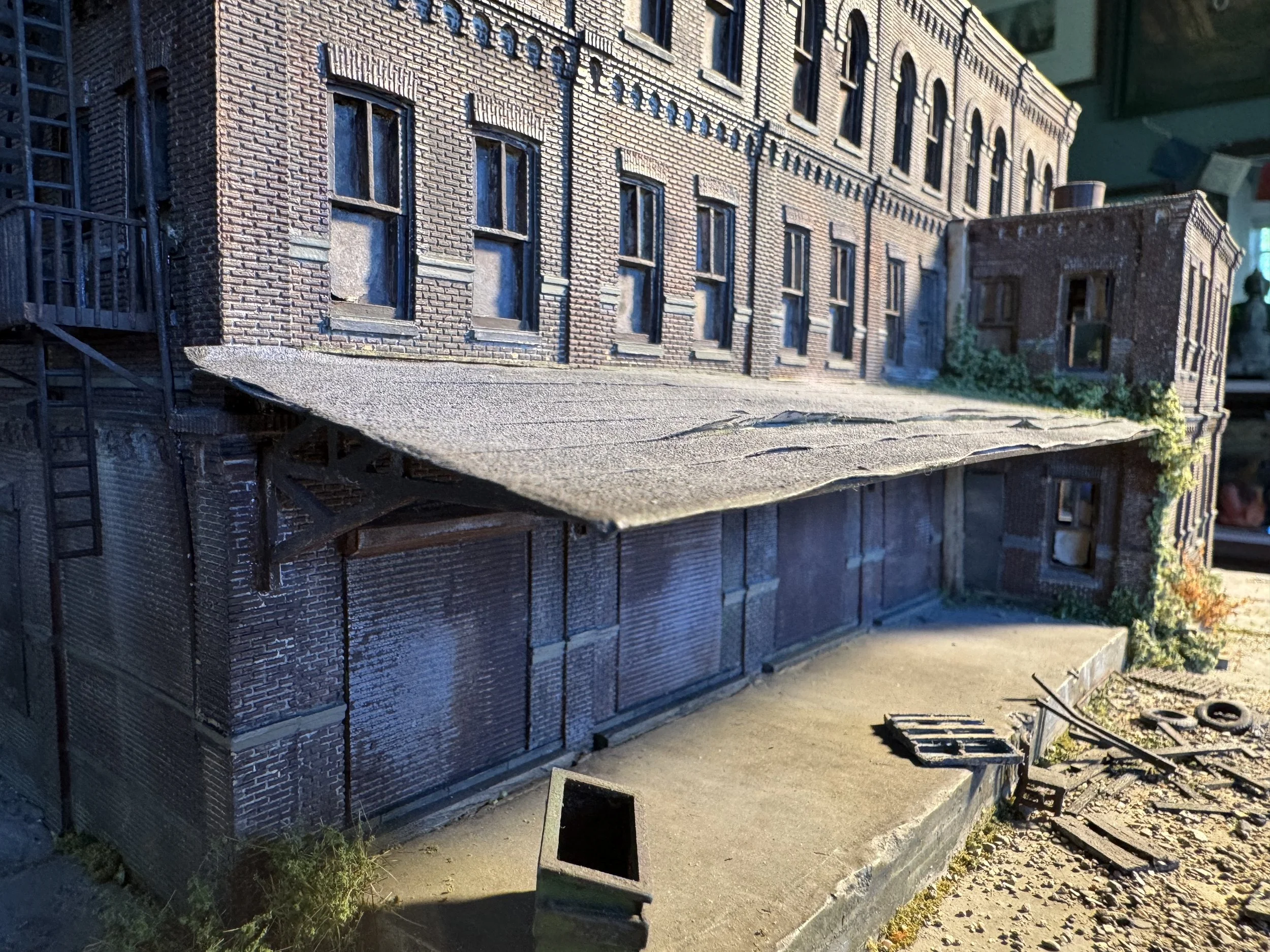 A detailed model of a brick building with multiple windows and a fire escape ladder on the side, situated on a paved area.