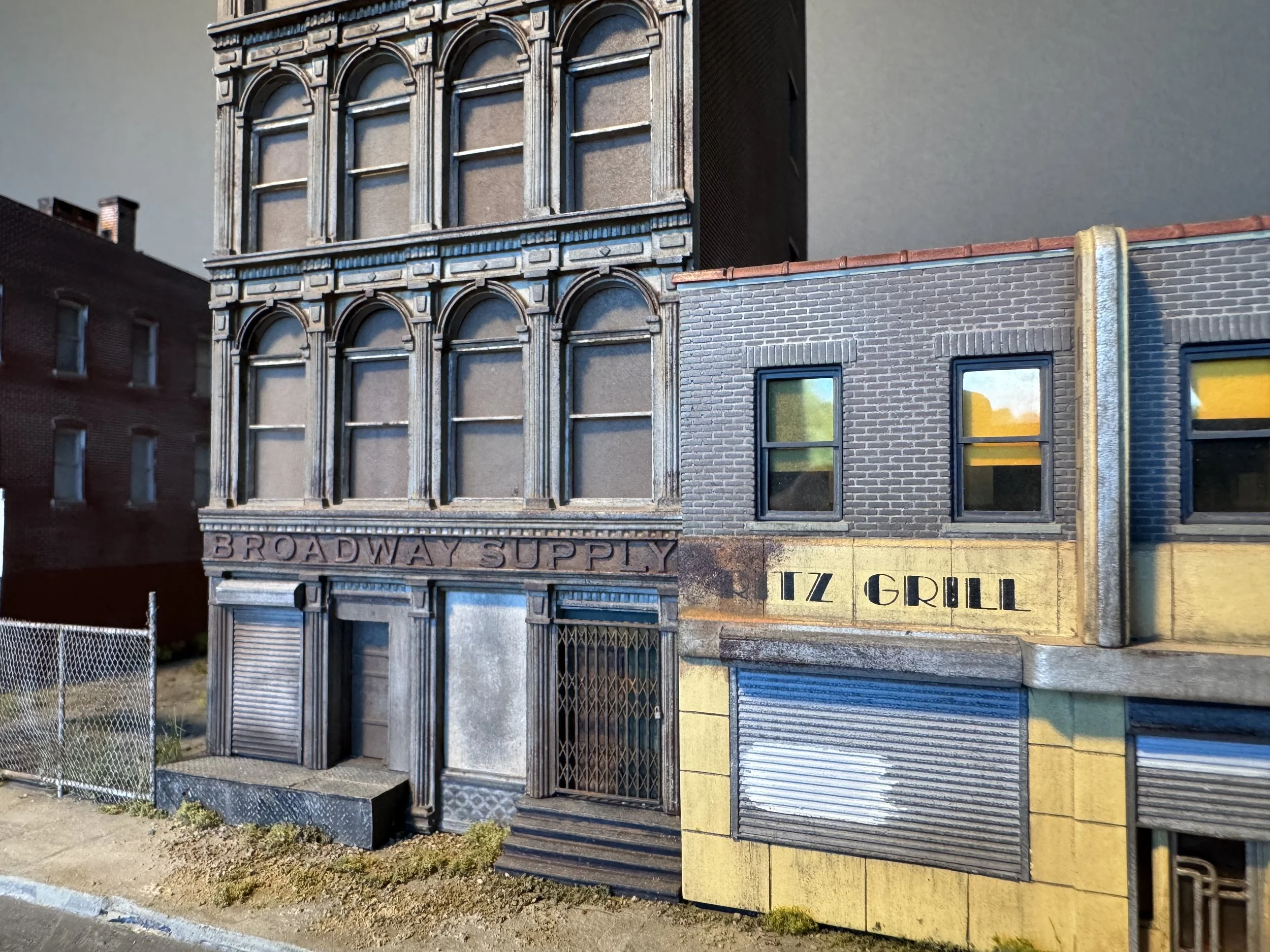 A building with a facade designed to resemble storefronts of old city shops, featuring detailed window and arch designs. The overall appearance is aged and weathered, with some parts looking like part of a miniature model or diorama.