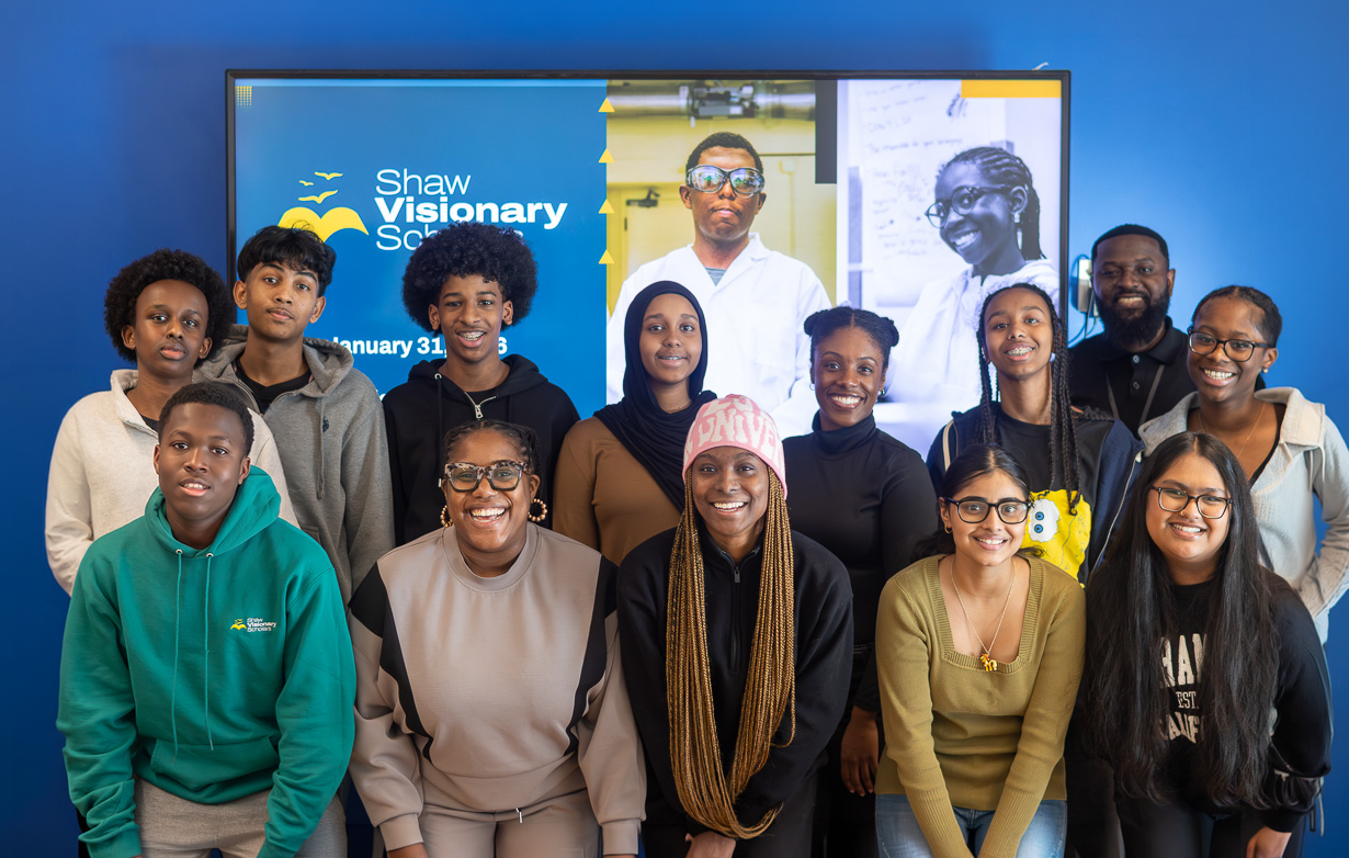The first cohort of youth scholars and leaders smiling together in front of a digital display at the Shaw Visionary Scholars program launch.
