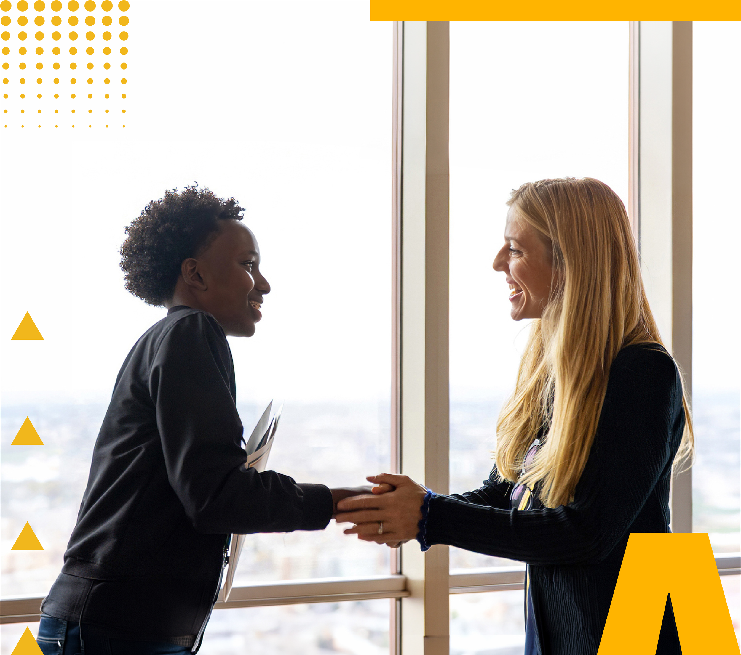 A youth scholar shaking hands and smiling with a program supporter in front of a window at the Shaw Visionary Scholars kickoff event.