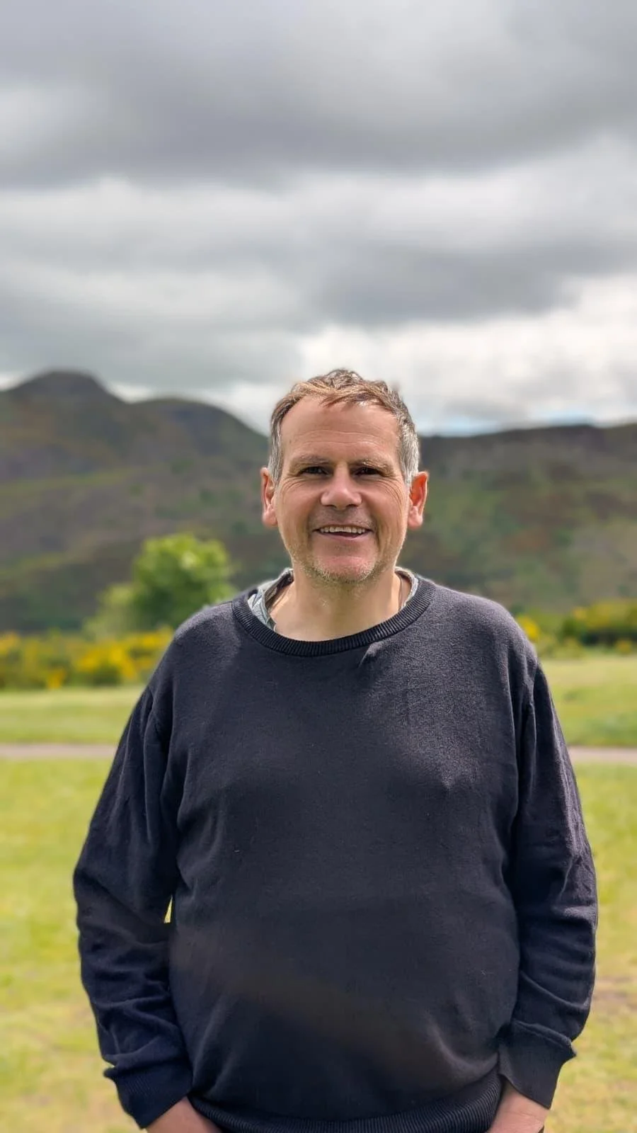 Jim standing on top of Calton Hill in Edinburgh with Arthurs Seat in the background