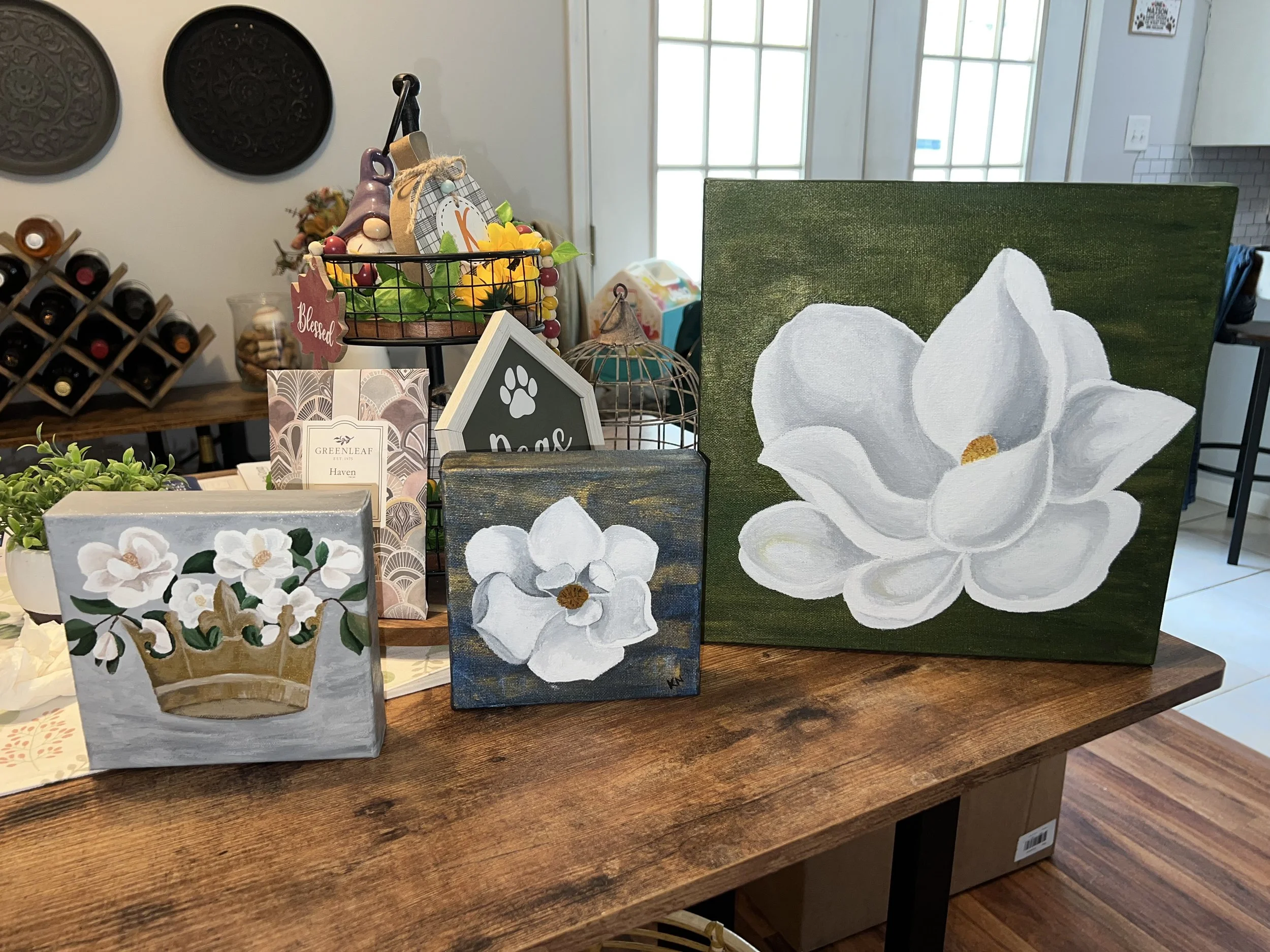 Collection of painted floral artwork on small canvases displayed on a wooden table.